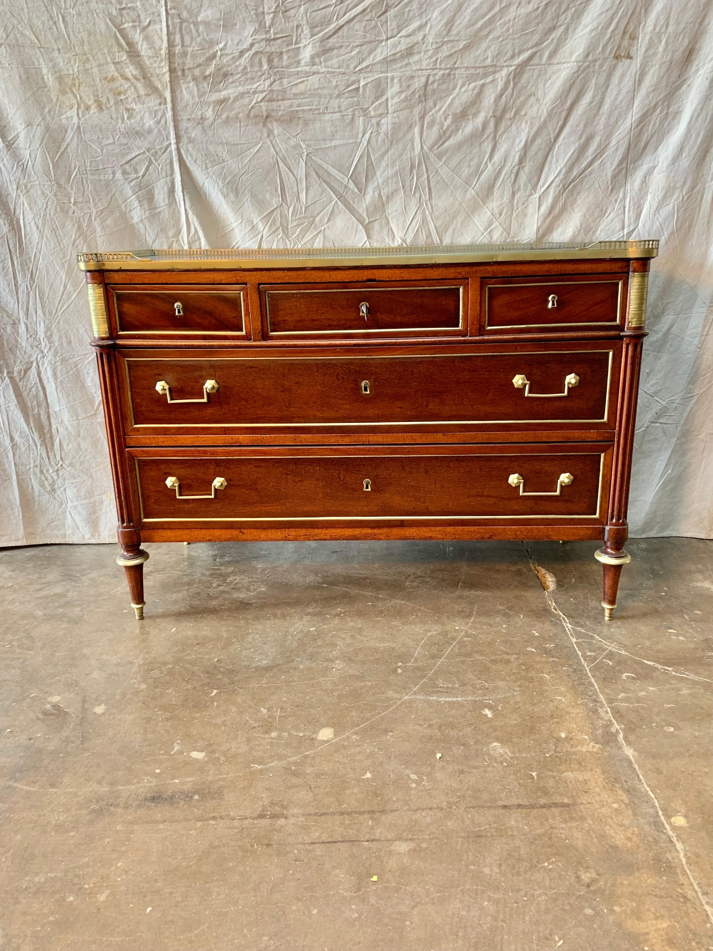 This 19th Century French Louis XVI Commode is made of mahogany and oak. The piece is crafted with a marble top and pierced brass gallery. The chest of drawers features five drawers on three rows, three small ones on the first row then two larger