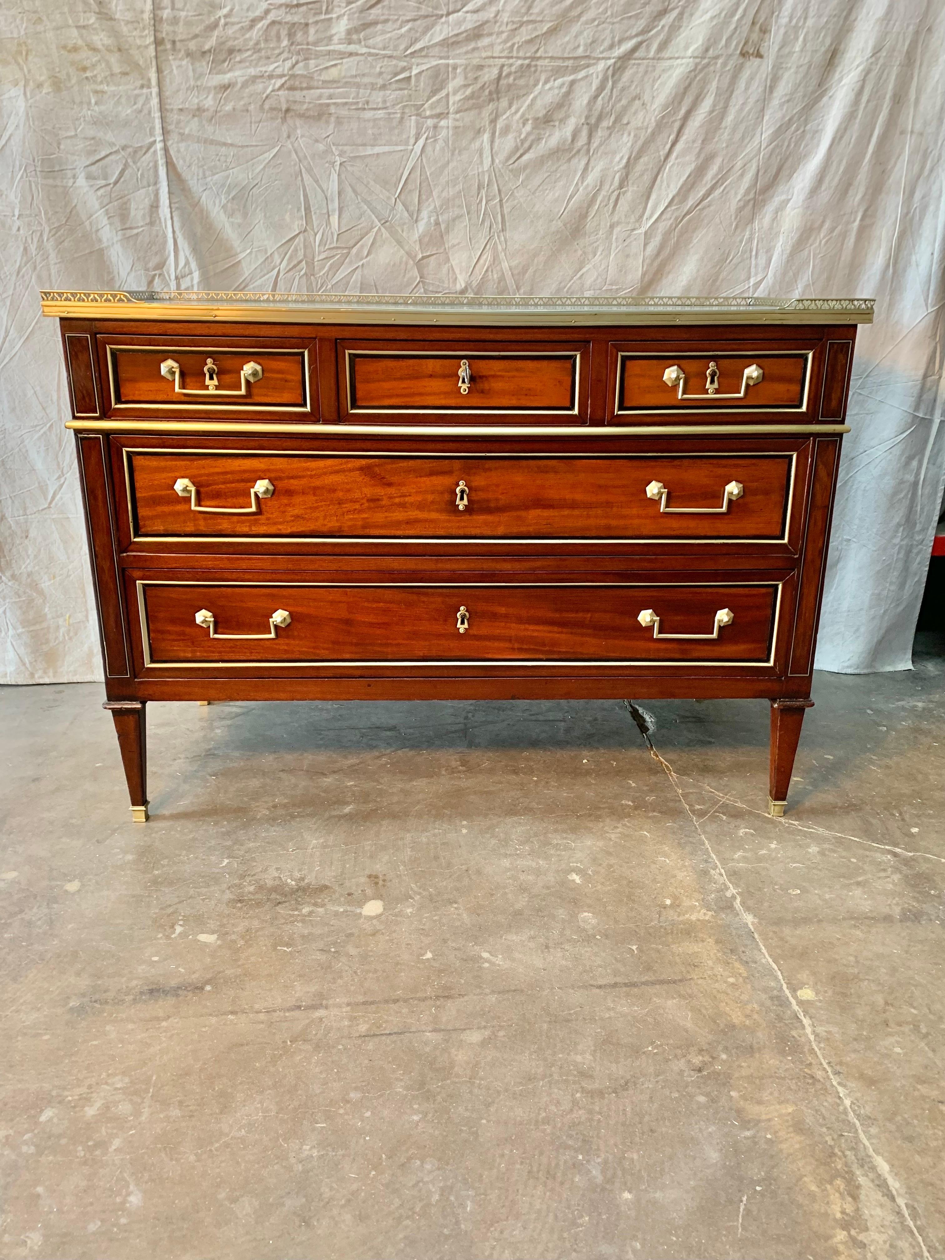 This 19th Century French Louis XVI Commode is made of mahogany and oak. The piece is crafted with a marble top and pierced brass gallery. Presented as found, repairs to the marble have been during the lifetime of the piece. The chest of drawers