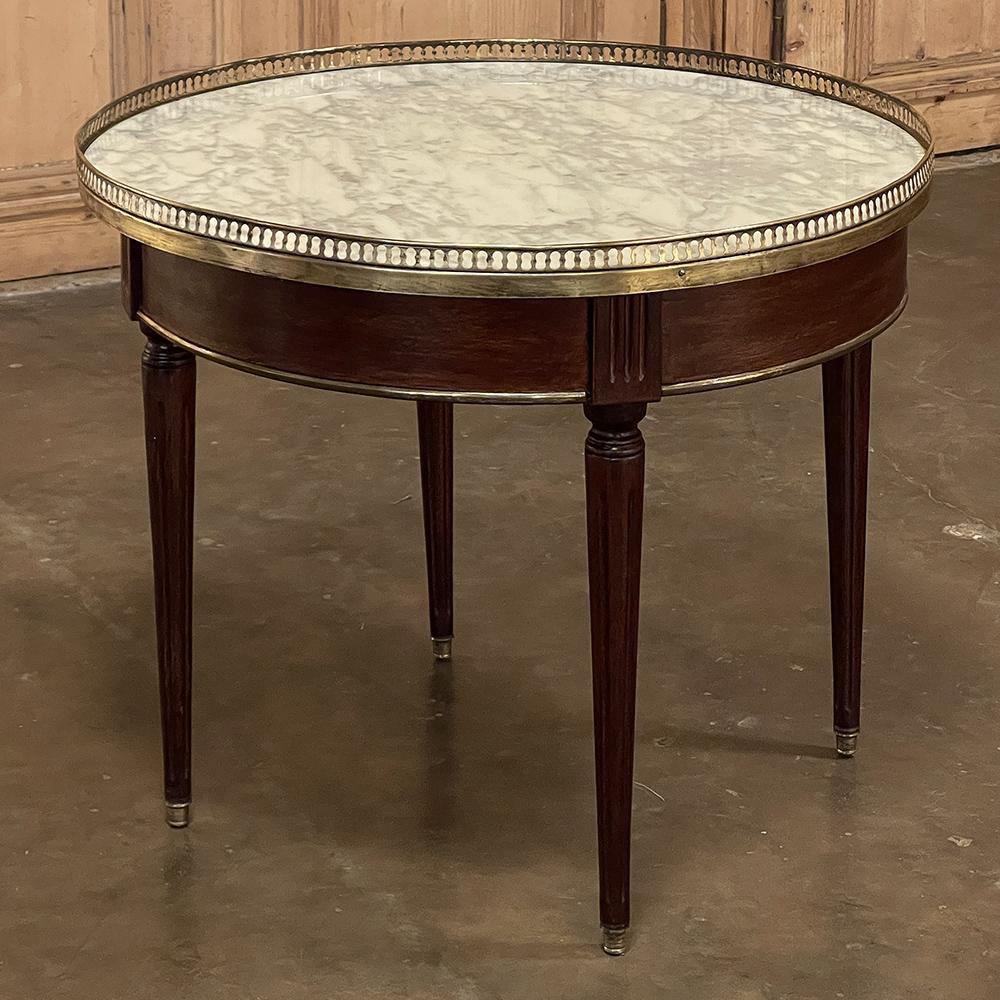 19th century French Louis XVI Mahogany marble top bouillotte table represents an understated elegance that is perfect for the tailored yet refined decor. Hand-crafted from exotic imported mahogany, it features a round apron interrupted by fluted