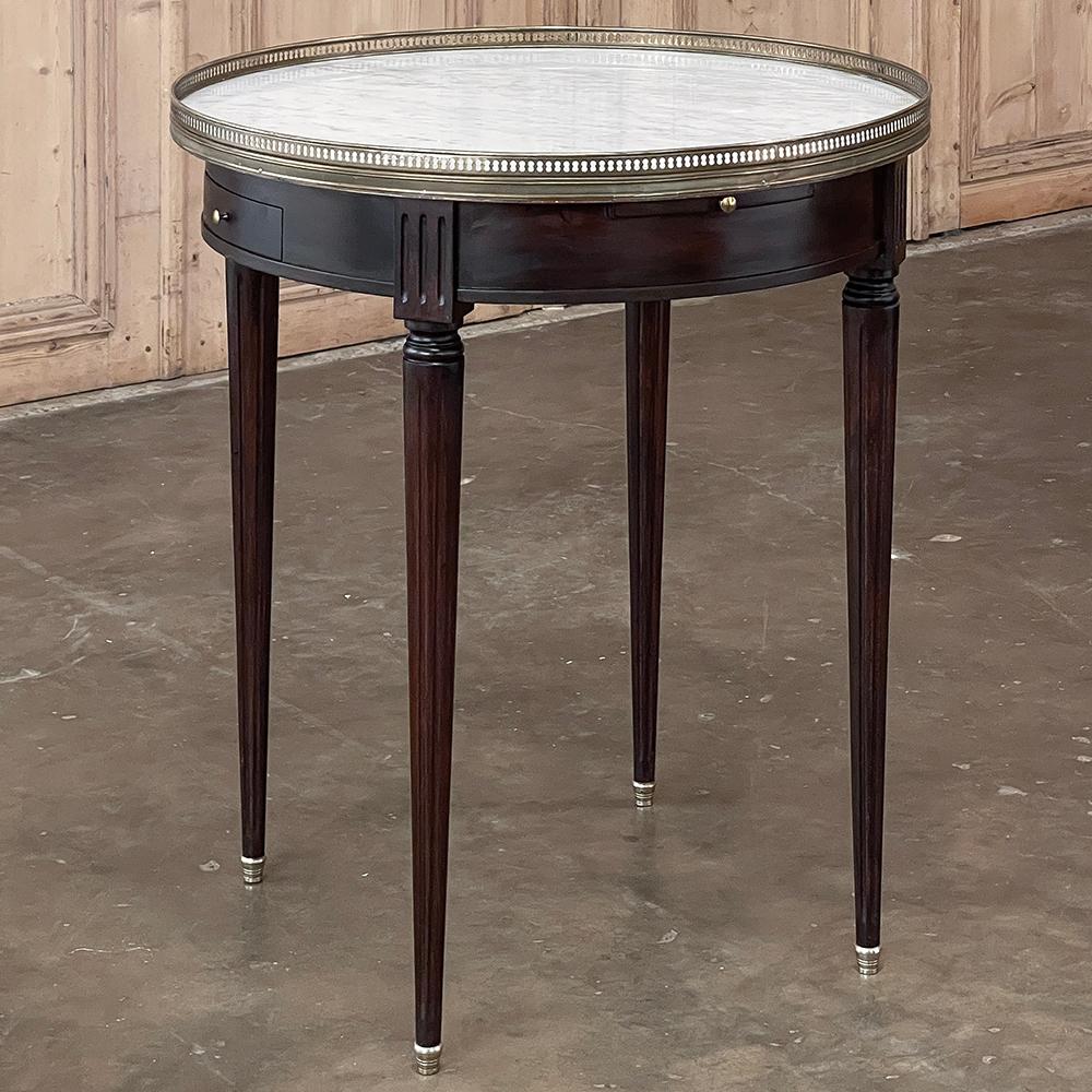 19th Century French Louis XVI Mahogany Marble Top Bouillotte Table represents an understated elegance that is perfect for the tailored yet refined decor. Hand-crafted from exotic imported mahogany, it features a round apron interrupted by fluted
