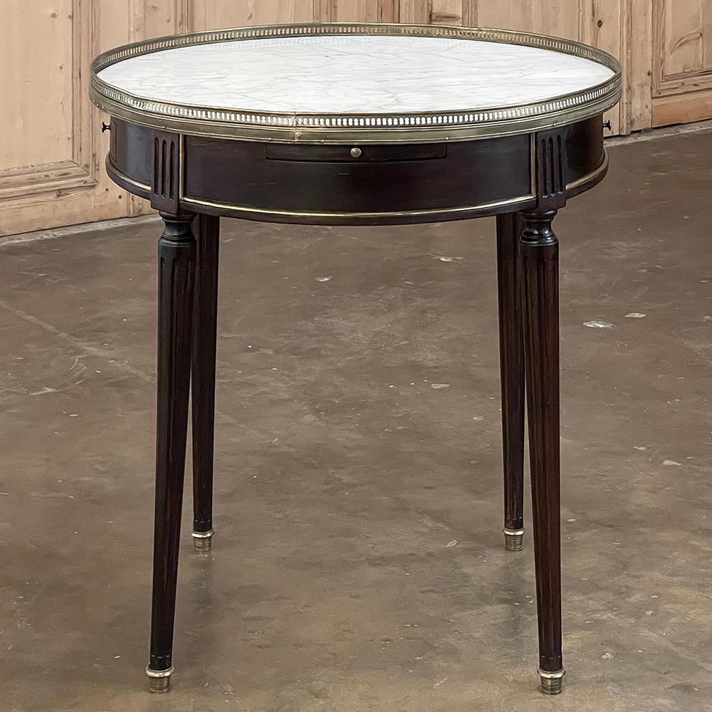 19th century French Louis XVI Mahogany Marble Top Bouillotte Table represents an understated elegance that is perfect for the tailored yet refined decor. handcrafted from exotic imported mahogany, it features a round apron interrupted by fluted