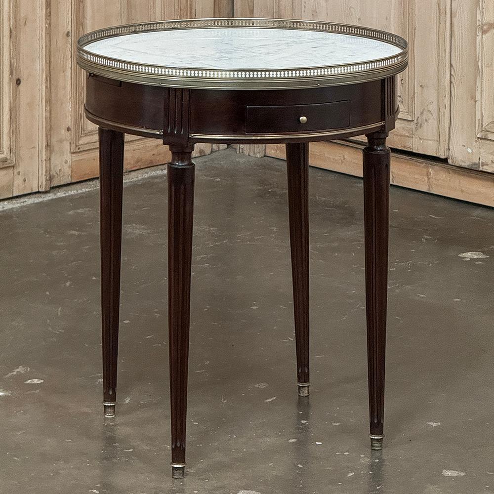 19th Century French Louis XVI Mahogany Marble Top Bouillotte Table represents an understated elegance that is perfect for the tailored yet refined decor. Hand-crafted from exotic imported mahogany, it features a round apron interrupted by fluted