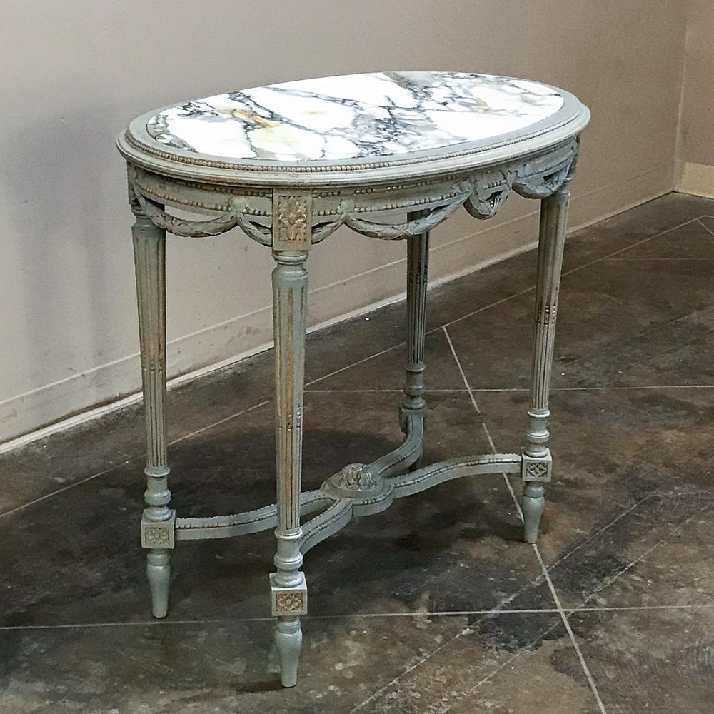 19th century French Louis XVI marble top painted end table features an oval shape that is pleasing to the eye, especially when one considers the hand carved neoclassical motifs of draped laurels, ribbon and beading enhanced by the patinaed painted