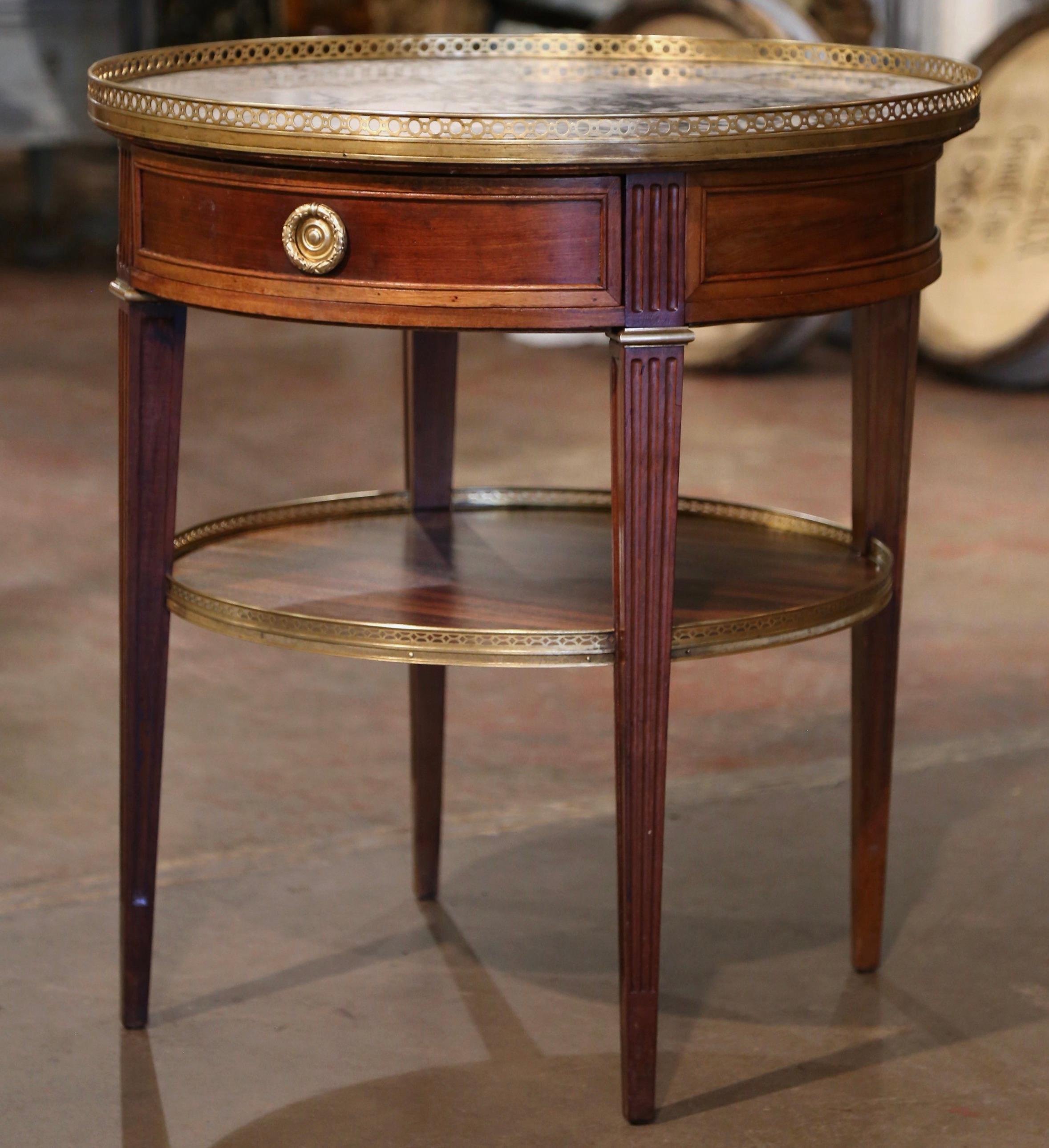 Use this elegant, antique fruit wood table in a living room or den as an occasional side table. Crafted in France, circa 1880, the bouillotte table stands on four tapered and fluted legs, decorated with a brass mount at the shoulder and features a