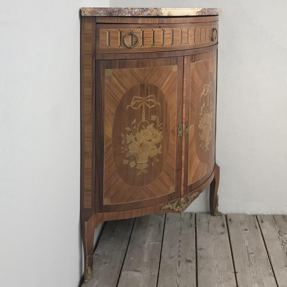 19th century French Louis XVI marquetry marble top corner cabinet is an exquisite way to take advantage of an otherwise unused corner! Handcrafted from Fine mahogany and inlaid in an artistic process known as marquetry depicting baskets bursting