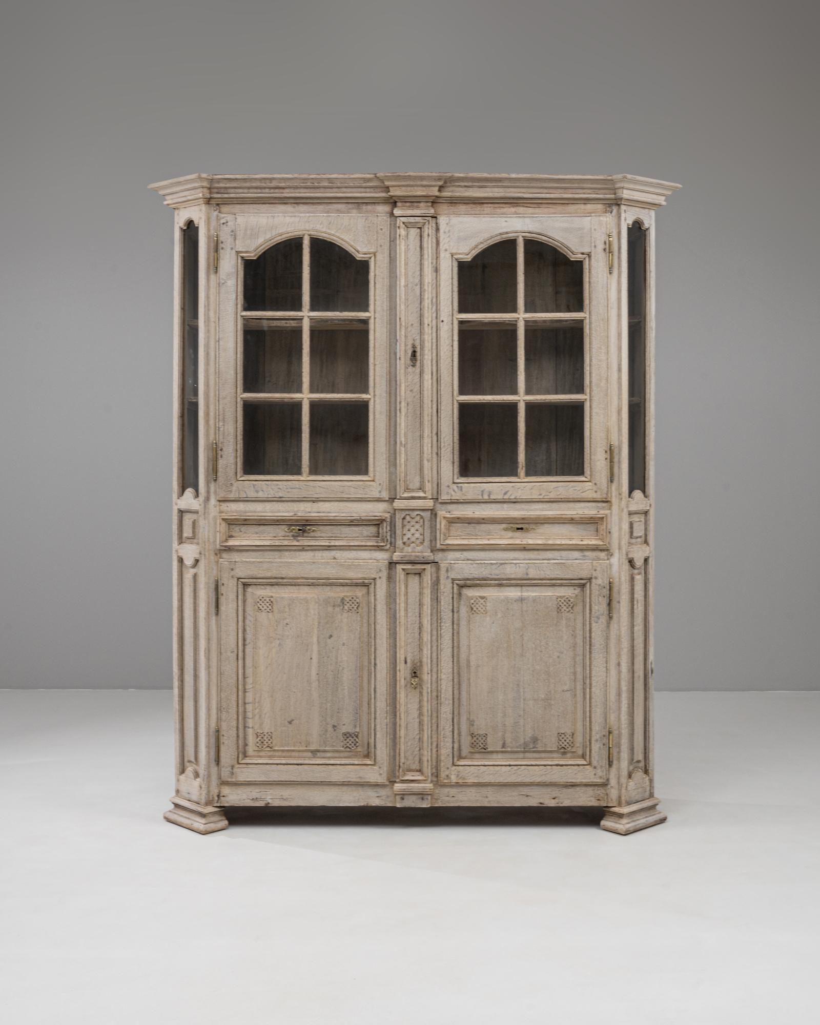 Diese französische Louis-XVI-Vitrine aus Eichenholz aus dem 19. Jahrhundert verkörpert mit ihren ausgewogenen Proportionen und fein geschnitzten Details eine raffinierte neoklassische Eleganz. Er ist aus Eichenholz mit einer sanften, verwitterten