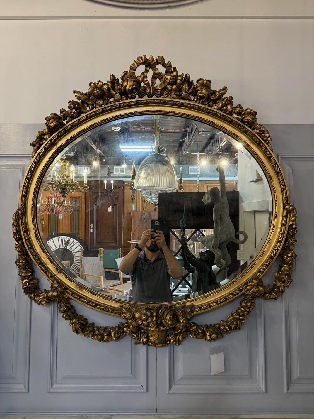 Exquis miroir ovale biseauté en bois doré de style Louis XVI français du 19e siècle. Avec ses belles sculptures et sa grande taille, ce miroir est impressionnant. Parfait au-dessus d'une cheminée ou d'une grande commode. Le miroir biseauté présente
