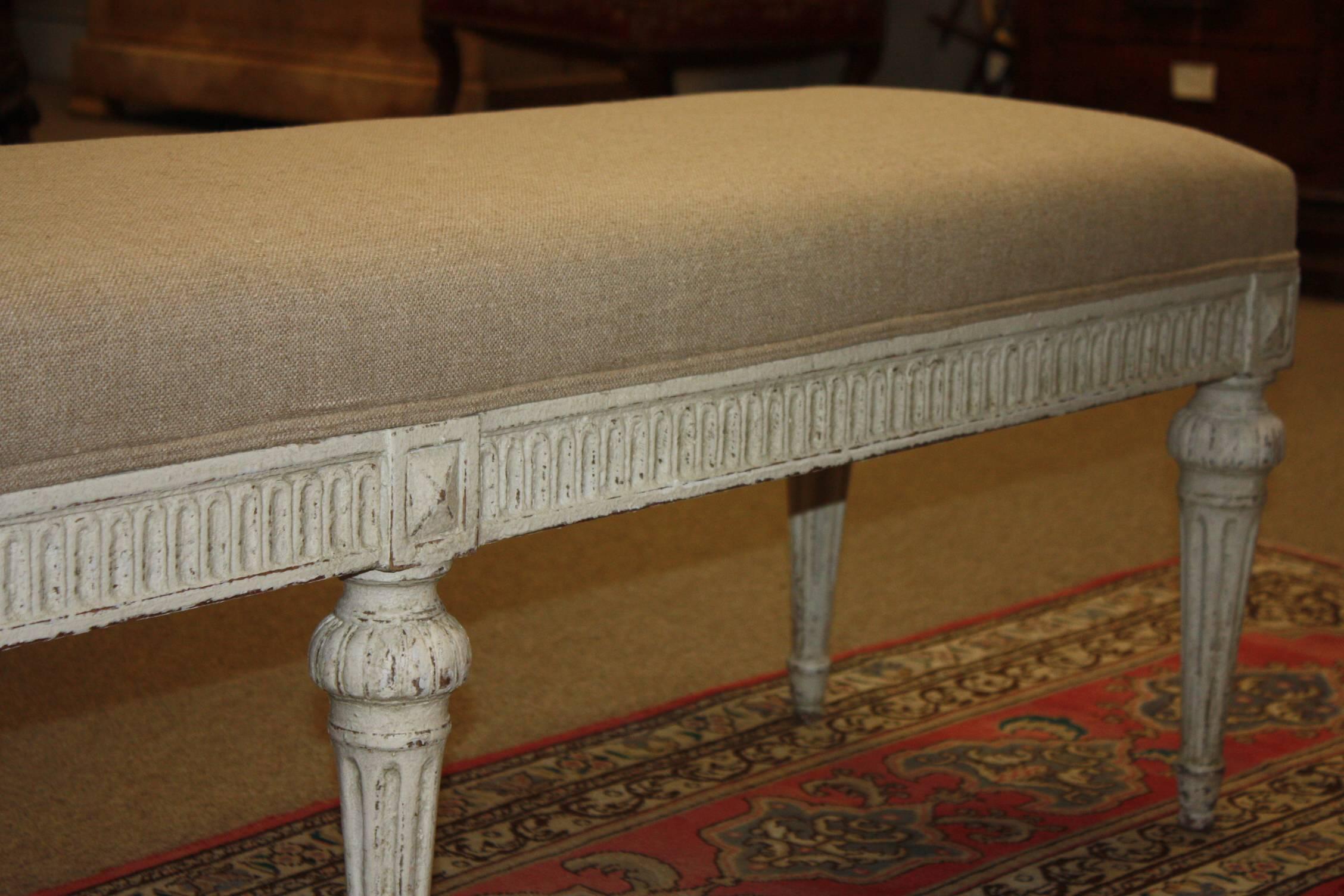 Louis XVI bench from France. Carved, circa 1880, the antique bench has six tapered legs, symmetrical carvings around the apron, and is reupholstered in a neutral. Due to its size and narrow profile, the bench would also make the perfect piece at the