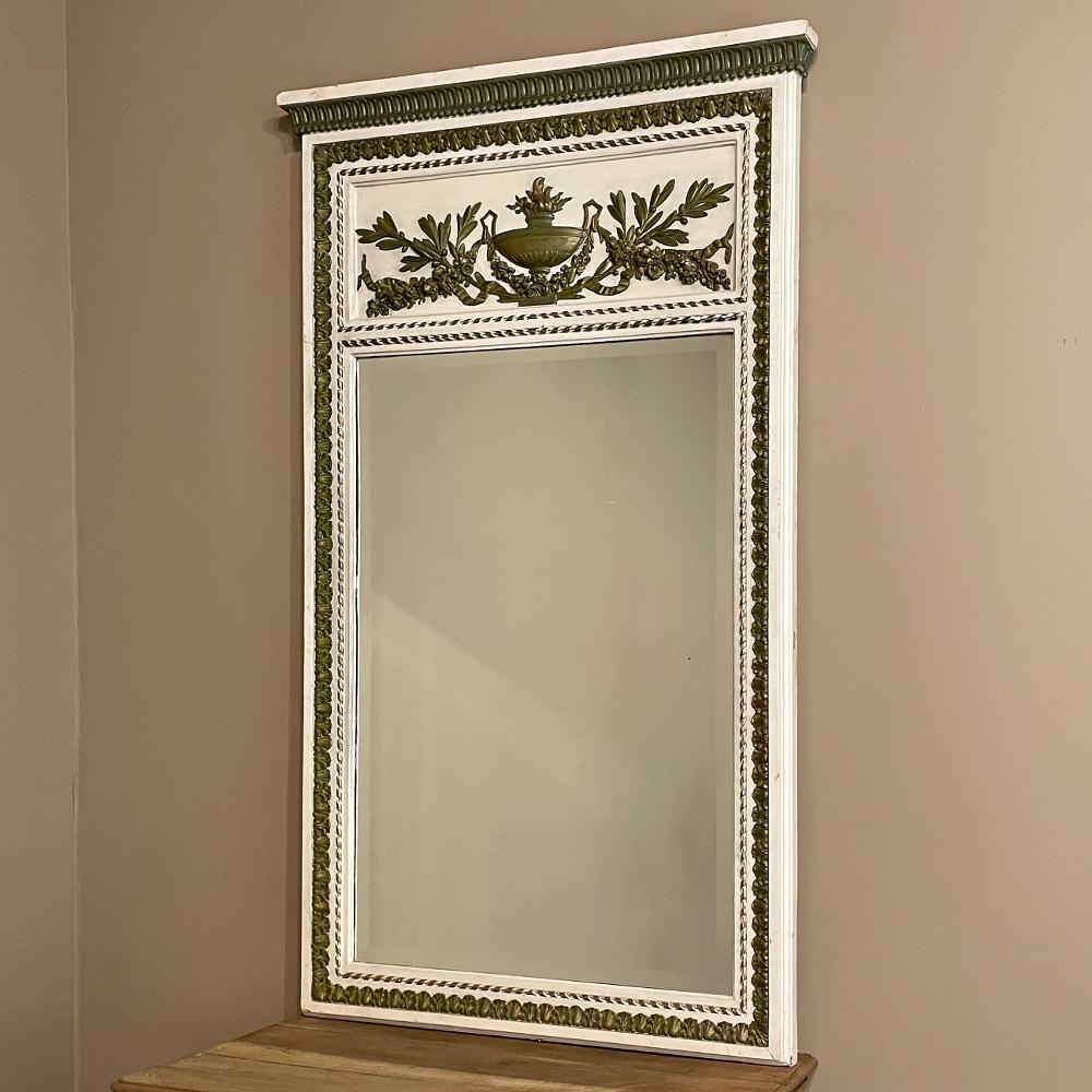 19th century French Louis XVI painted & gilded trumeau mirror features exquisite relief carvings on the panel above the generously sized beveled mirror depicting an eternal flame emanating from a Grecian urn flanked by floral swags and olive