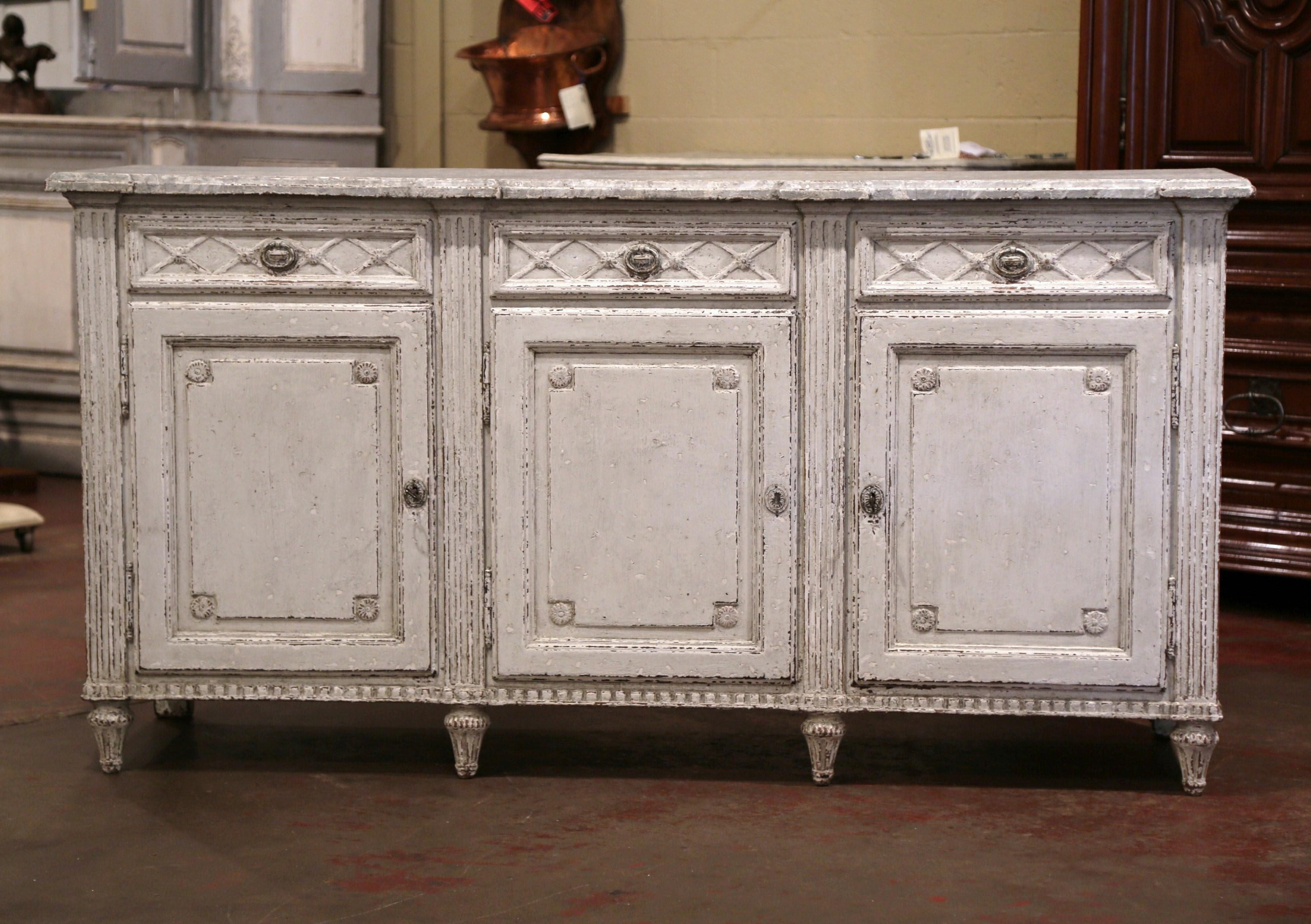 Crafted in France circa 1870, the antique grey painted sideboard stands on eight turned and tapered legs over a straight and carved apron. The traditional enfilade features three doors across the front; each door with inset panel, is decorated with