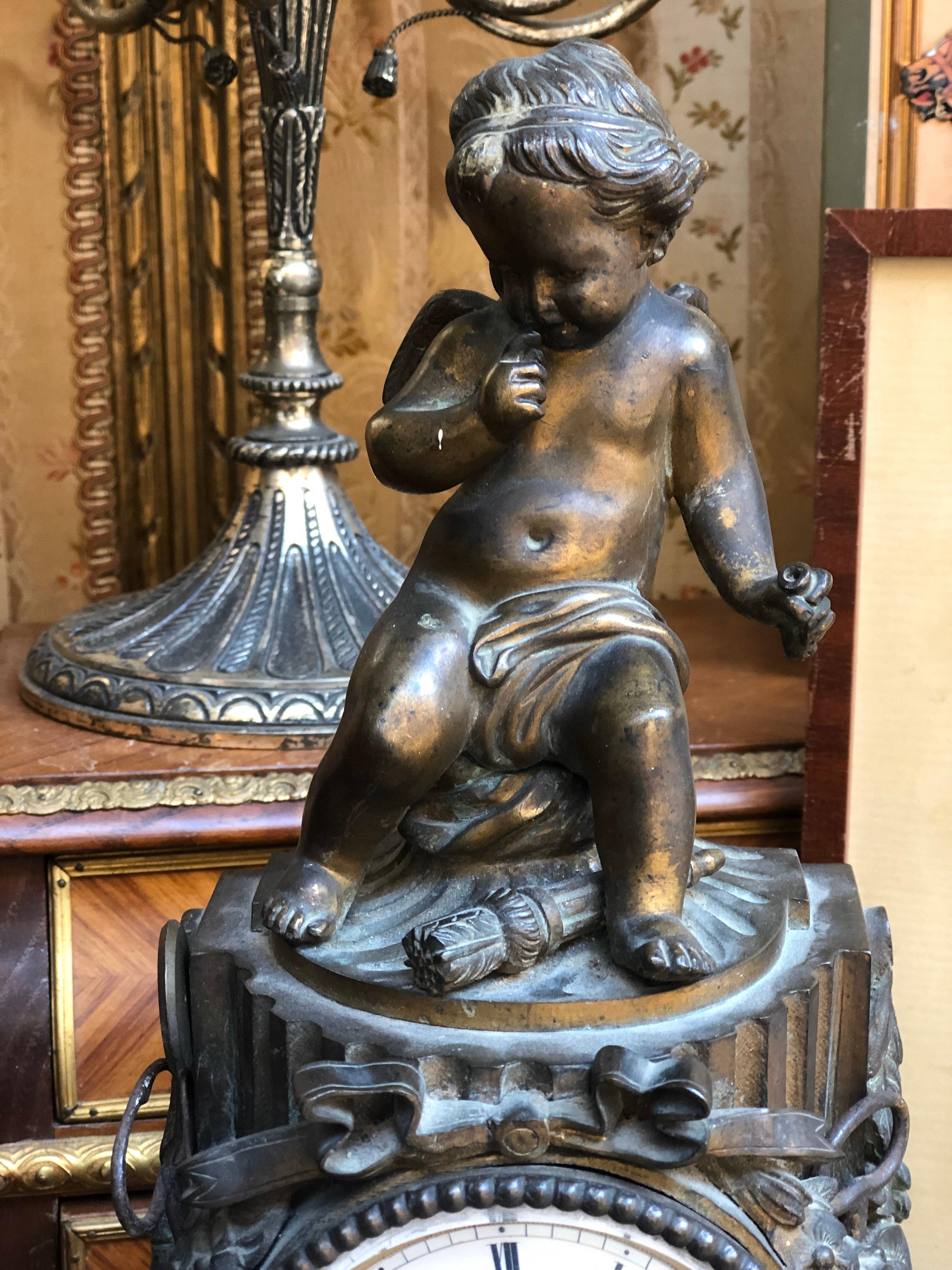19th century French antique bronze desk or mantel clock dated circa 1870. The clock stands on curved base and features a carved sculpture of a seating cupid. The intricate clock mechanism has been cleaned and checked and is in wonderful working