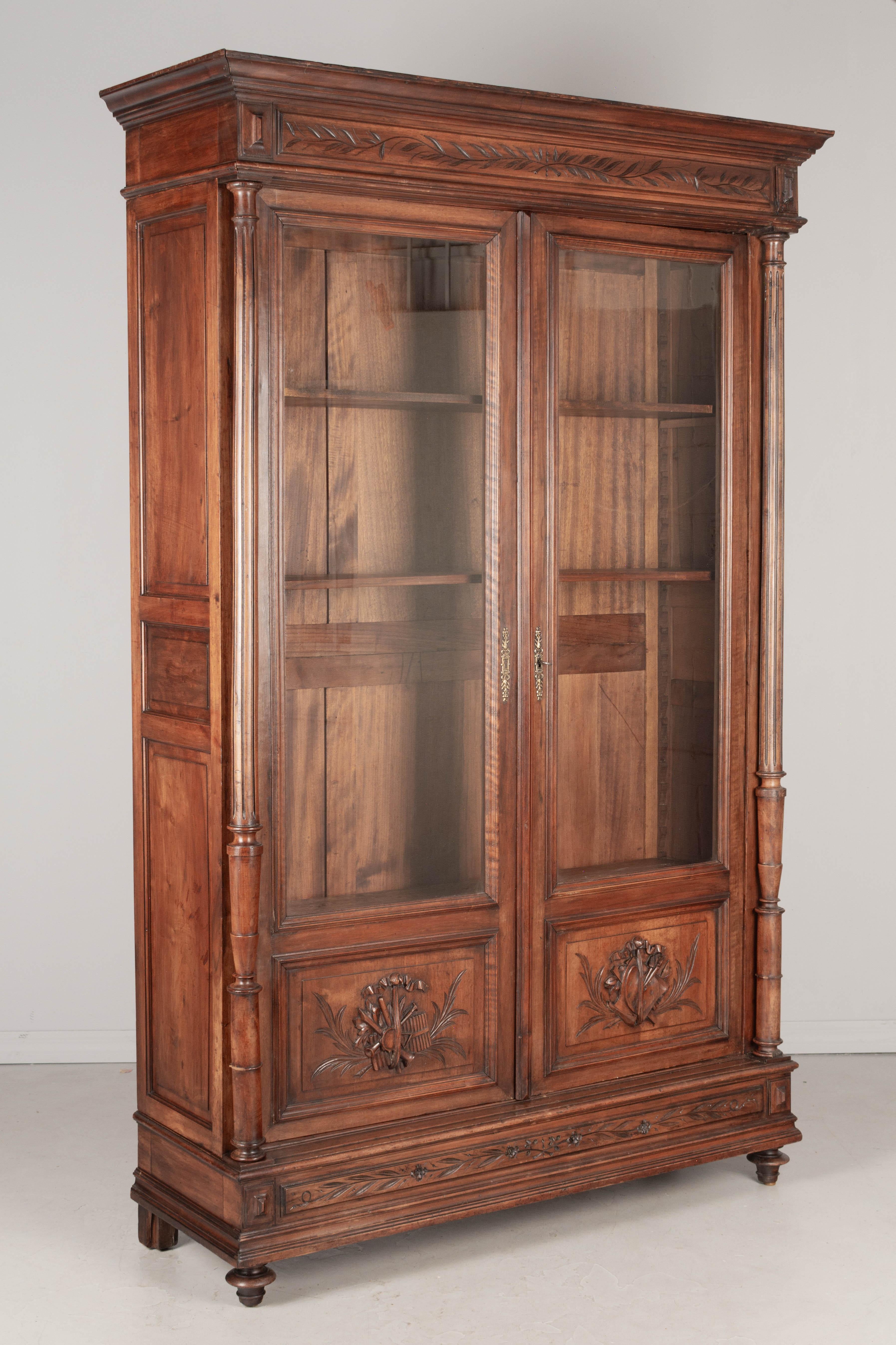 A 19th century French Louis XVI bibliotheque, or bookcase, made of solid walnut with mahogany as a secondary wood. Nice hand carved decorative panels at the bottom with musical instruments on the left and an artist's palette on the right. Turned