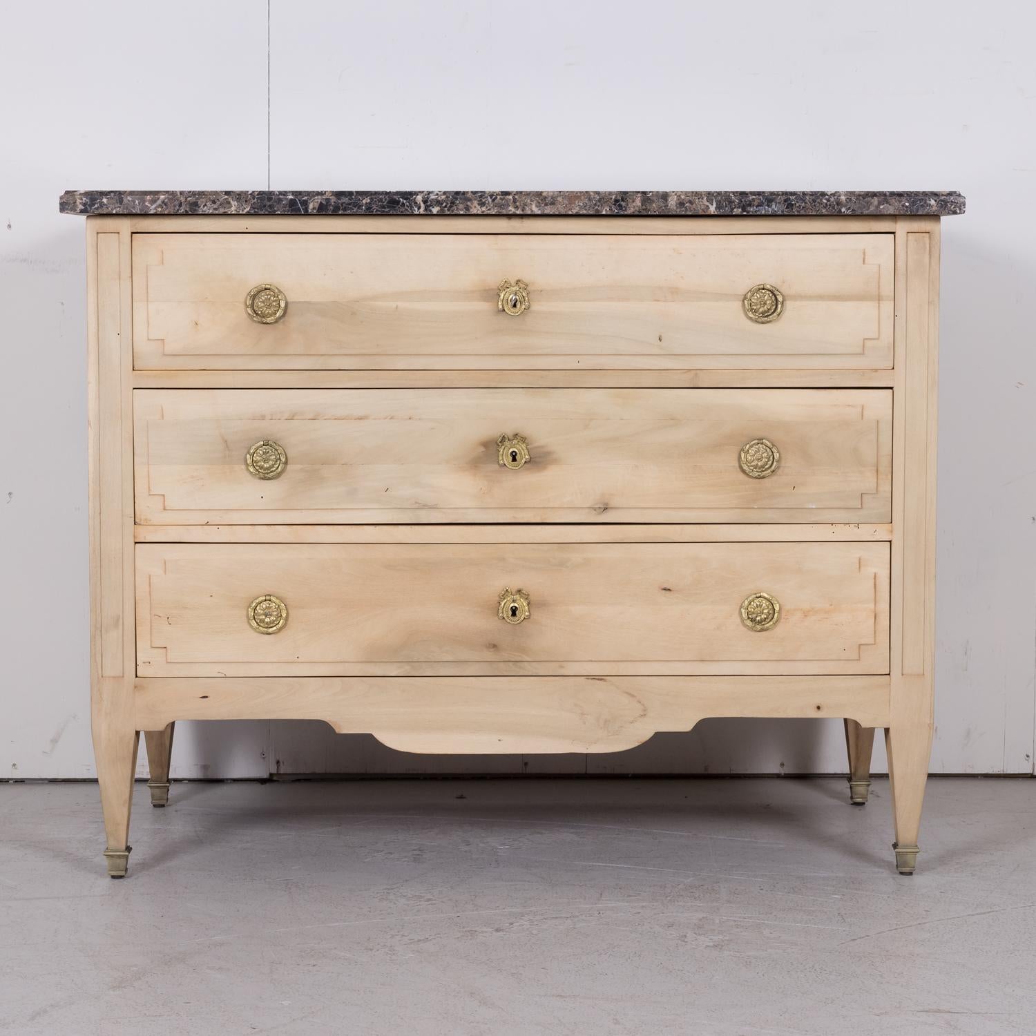 19th century French Louis XVI style bleached cherry commode, circa 1880s, having a beautiful dark emperador marble top above three drawers adorned with original brass neoclassical pulls and ribbon escutcheons. Raised on short tapered legs ending in