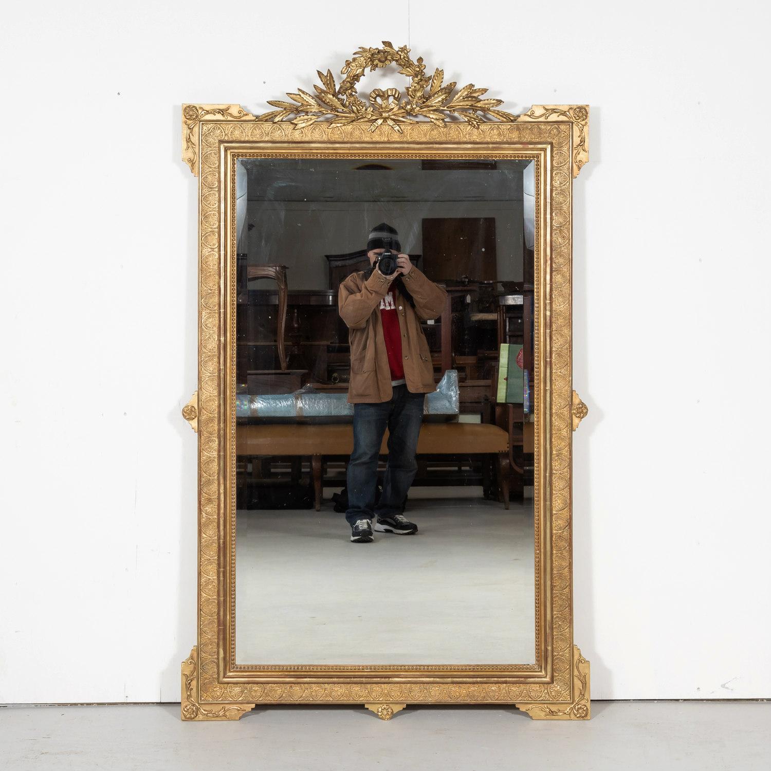 Ornate 19th century French Louis XVI style giltwood mirror, circa 1840s. This large, neoclassical mirror, having a richly carved giltwood frame, features typical elements of the Louis XVI period. The intricately carved and pierced crown depicts a