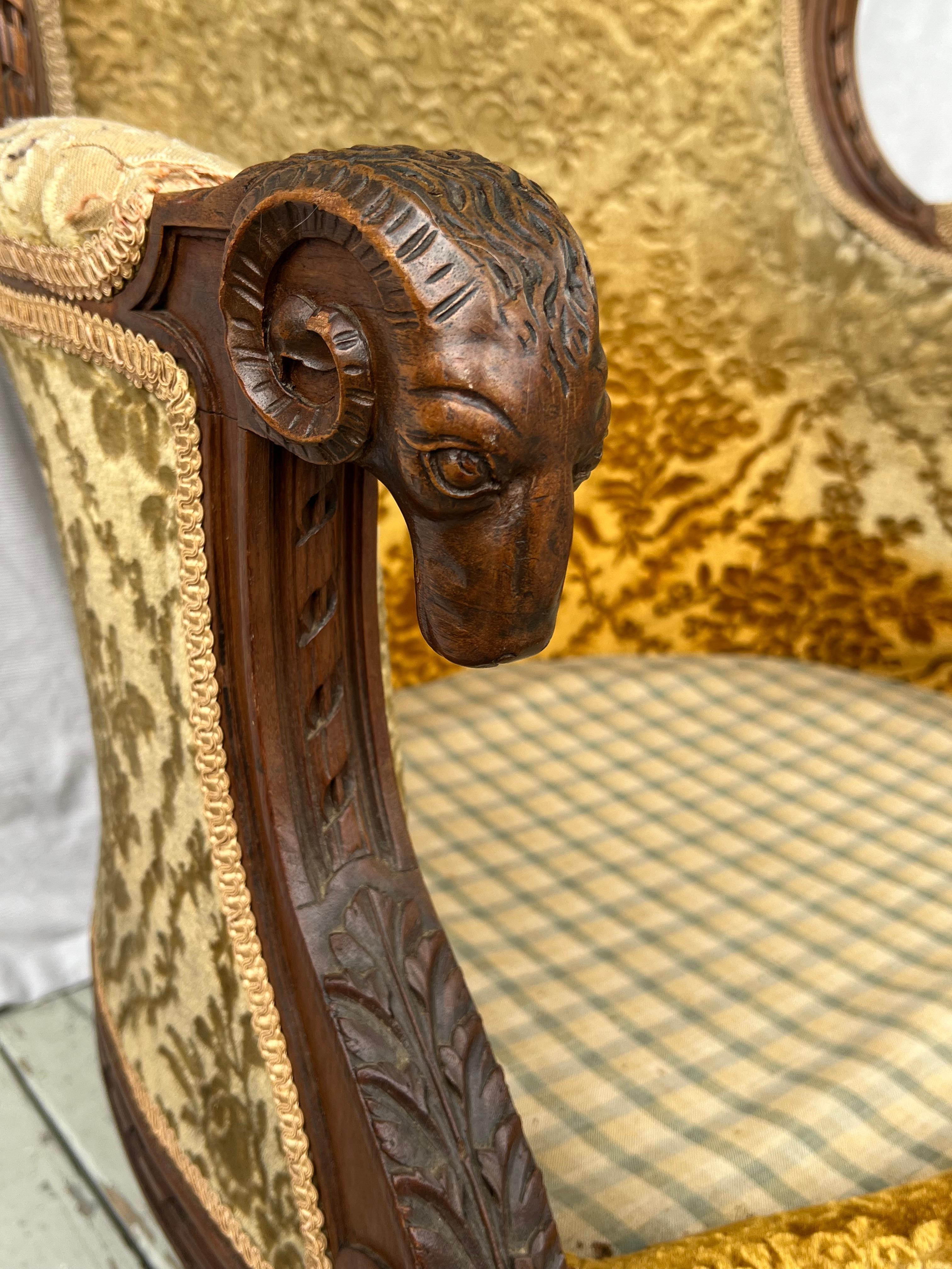 A large 19th century French carved walnut Bergere armchair in the Louis XVI style. 
This beautifully carved bergere has rams heads carved flowers, gadrooning and round tapering fluted legs.  It does not have a seat cushion but it decks at 13