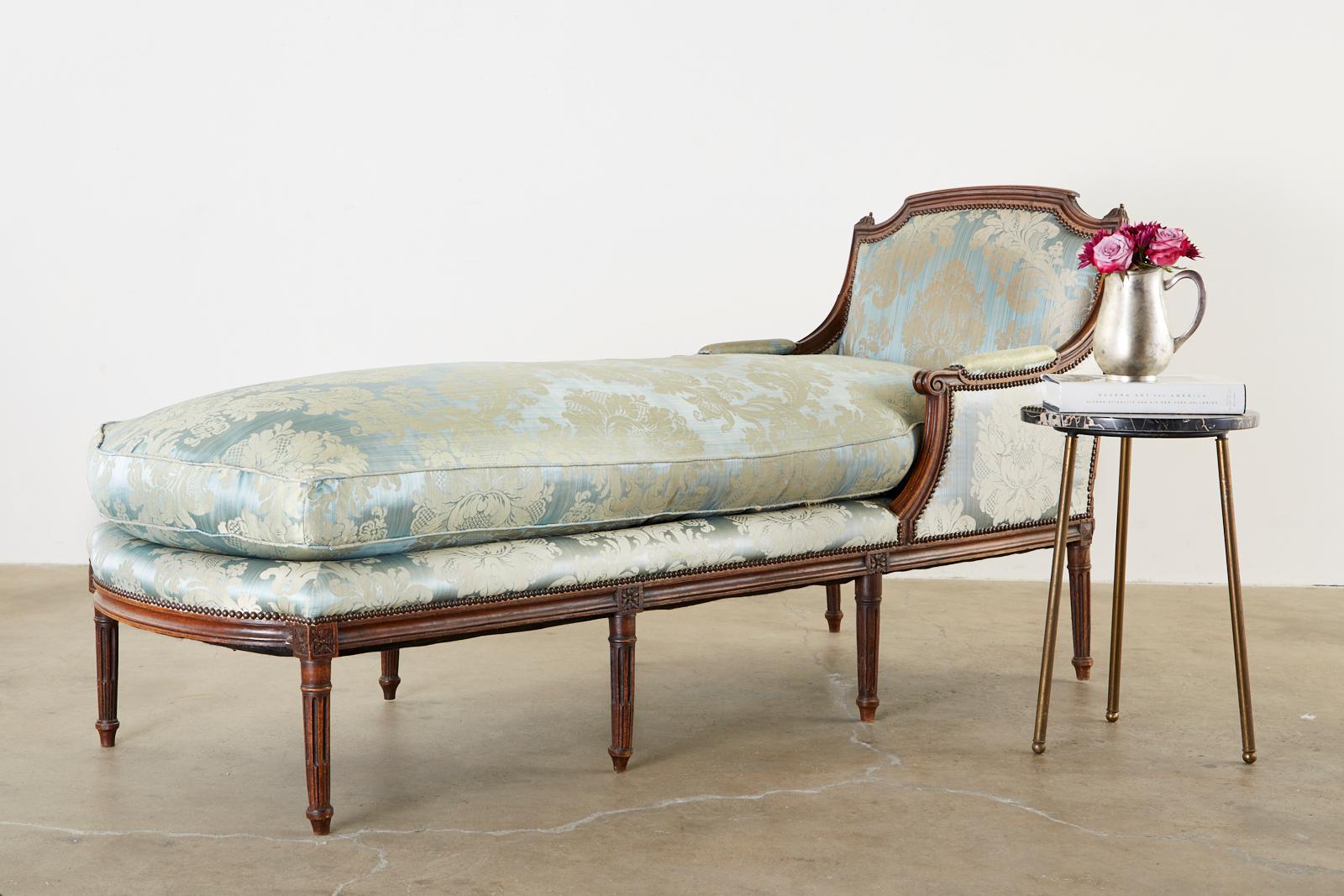 Gorgeous 19th century French chaise lounge or daybed made in the Louis XVI taste. Features a hand carved walnut frame with a flat back an arched crest rail. The arms gracefully curve down ending with scrolls and attach to a large seating area topped