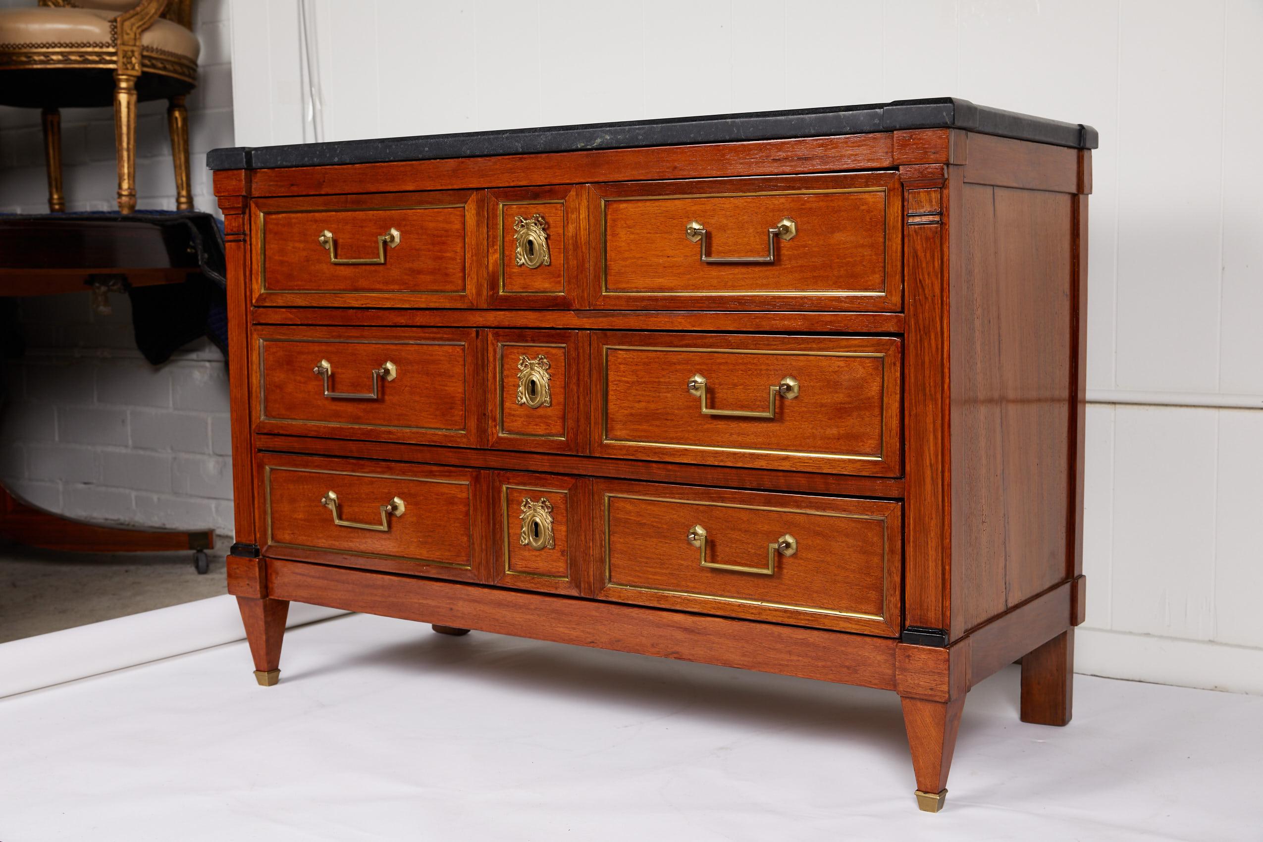 Mid-19th century French commode constructed in the manner of Louis XVI with a beautiful top of gray soapstone over a walnut case containing three drawers. Each drawer is inlaid with brass and has ribbon escutcheons and rectangular brass bail
