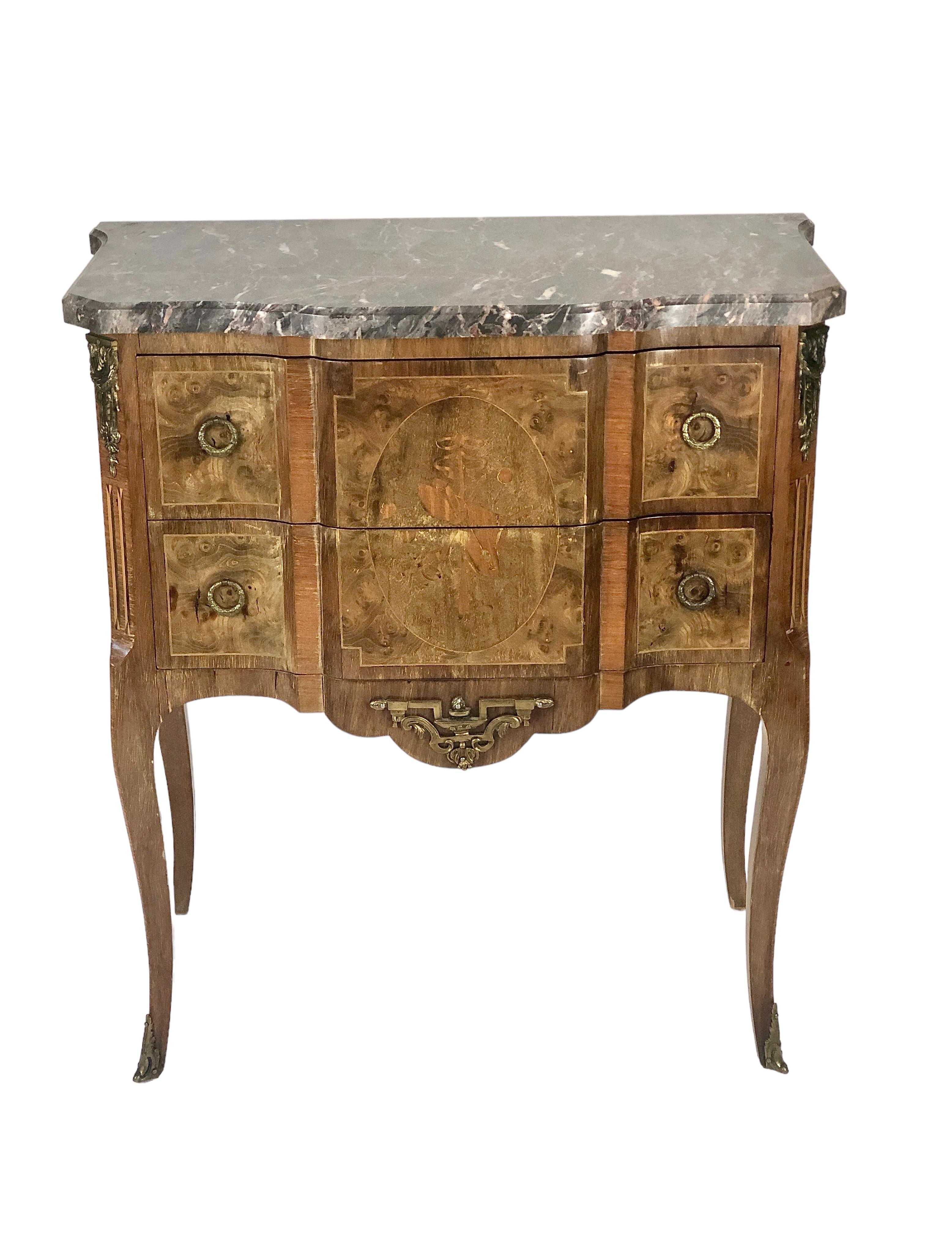 Delicata commode francese del XIX secolo in stile Luigi XVI, impiallacciata di intarsio con piano in marmo grigio. I suoi due cassetti, con sporgenza centrale, sono ornati da maniglie in bronzo e da un'intricata decorazione di strumenti musicali in