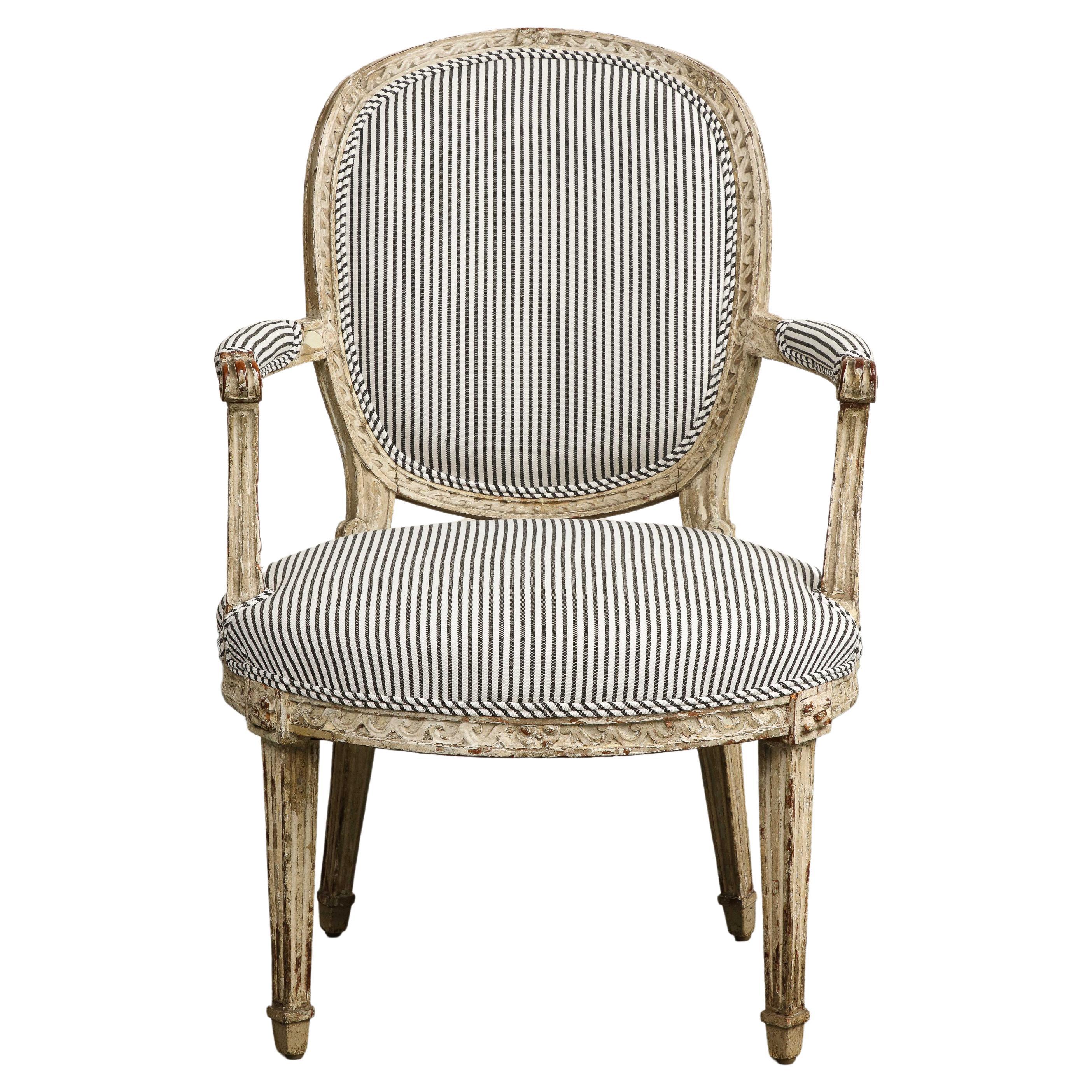 19th Century French Louis XVI Style Fauteuil armchair, with carved tapered legs, retaining old traces of paint over exposed wood. New striped linen upholstery done in 2022, with self-welt edges; the chair has not been used with the new fabric.