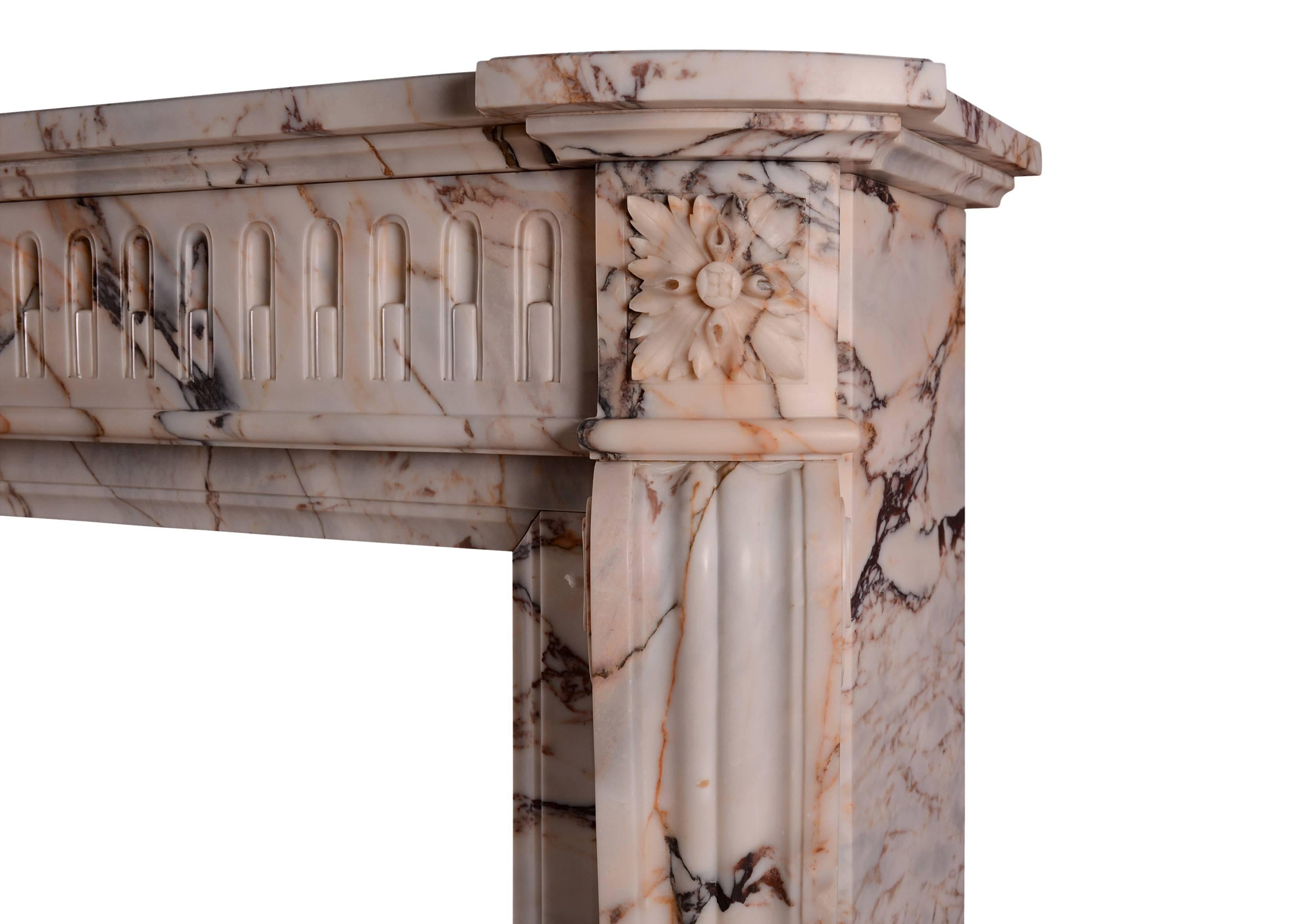 An unusually high French marble fireplace in the Louis XVI manner. The shaped jambs surmounted by carved square paterae, the bowed frieze with stop-flutes throughout. Shaped moulded shelf above. A veined marble from the Greek island of Skyros,