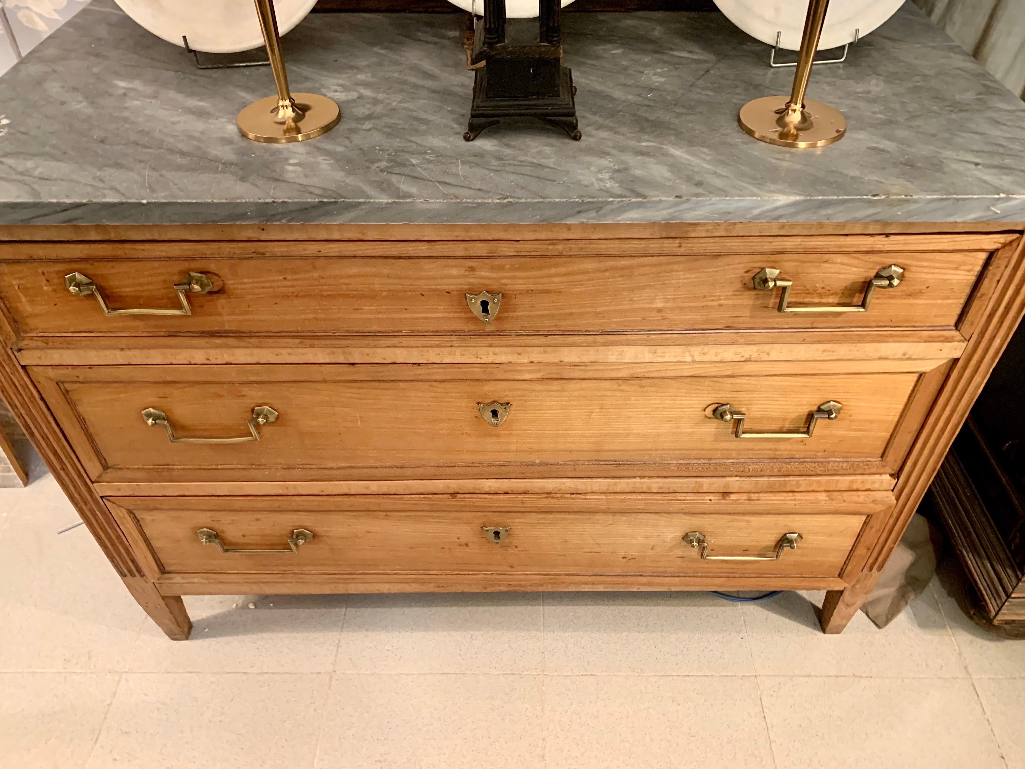 A chest of drawers from the early 19th century, which continues the Louis XVI style, in fruit wood with three drawers and a gray veined marble top.
the handles are bronze, two of them slightly smaller, the sides of the chest of drawers in ribbed