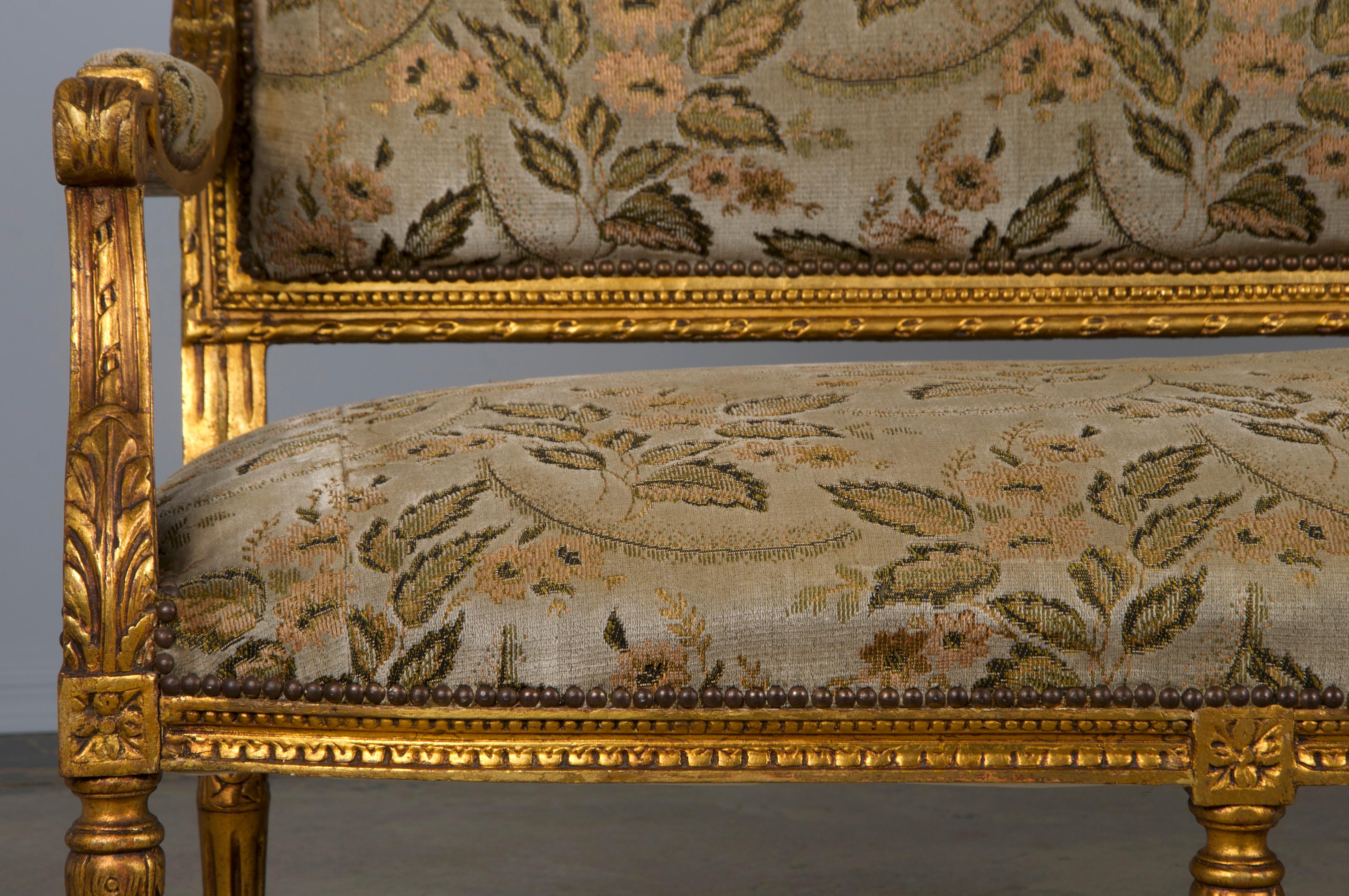 An exquisite mid-19th-century French 3-seater settee sofa made in the style of Louis XVI, sourced from Provence, France. Handcrafted from solid gilded wood, the settee boasts a solid hand-crafted frame with a square-shaped back featuring intricately