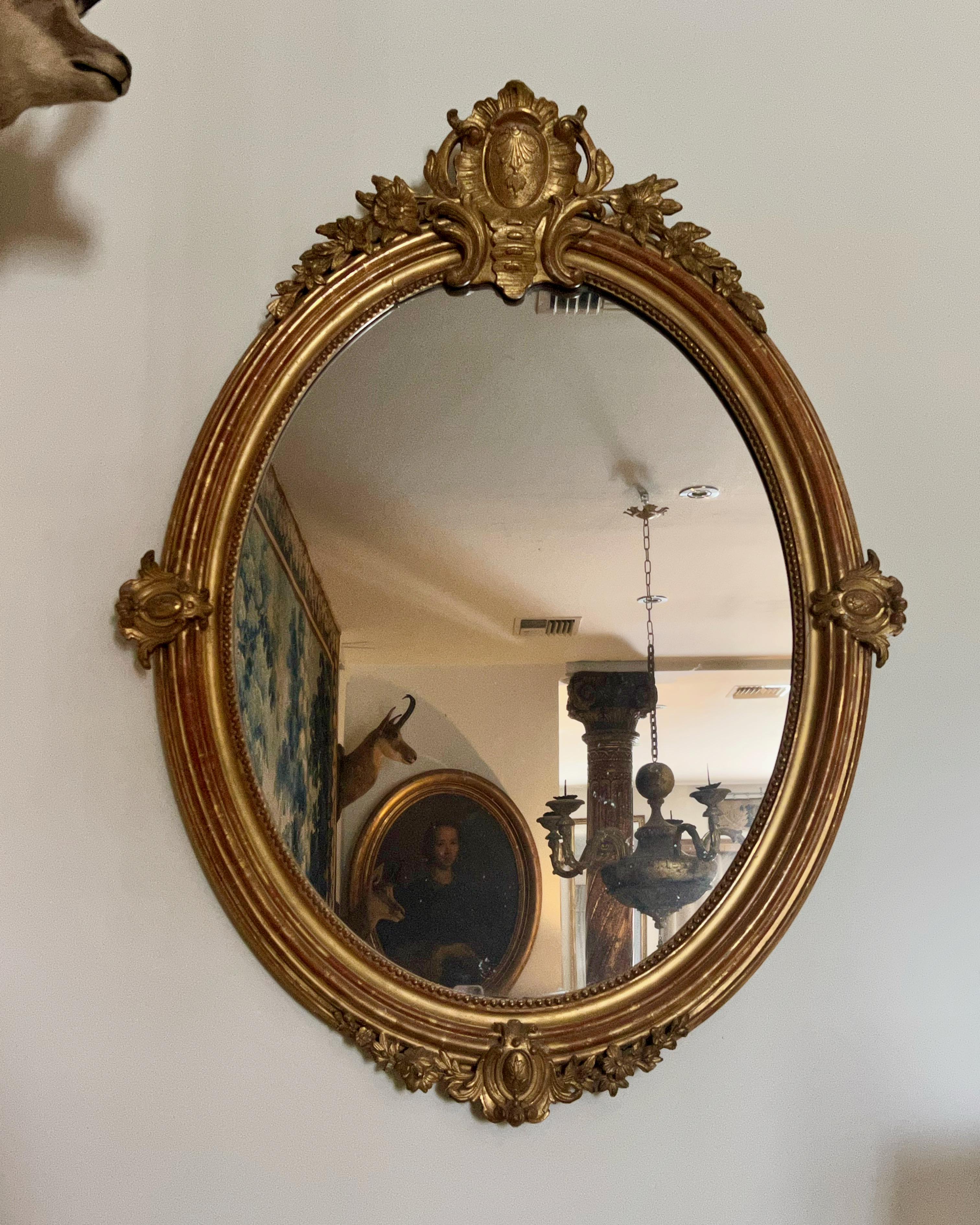Miroir doré de forme ovale de style Louis XVI français du 19e siècle, avec plaque de miroir d'origine et cadre doré patiné d'origine avec des sculptures finement détaillées.
France 19ème siècle.