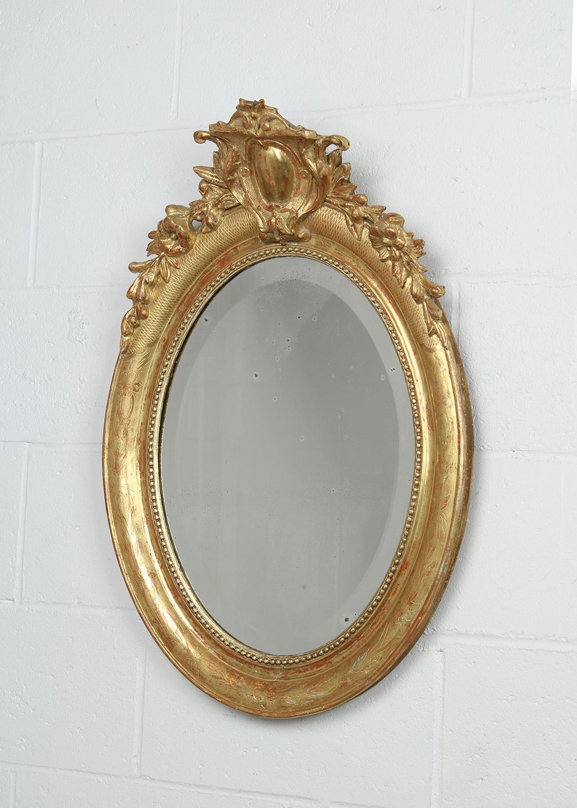 Immerse yourself in the elegance of the 1840s with our French Louis XVI-style gilt oval mirror. The mirror is beautifully framed with intricate floral designs, all meticulously carved and crowned. The water gilt finish further enhances its allure.