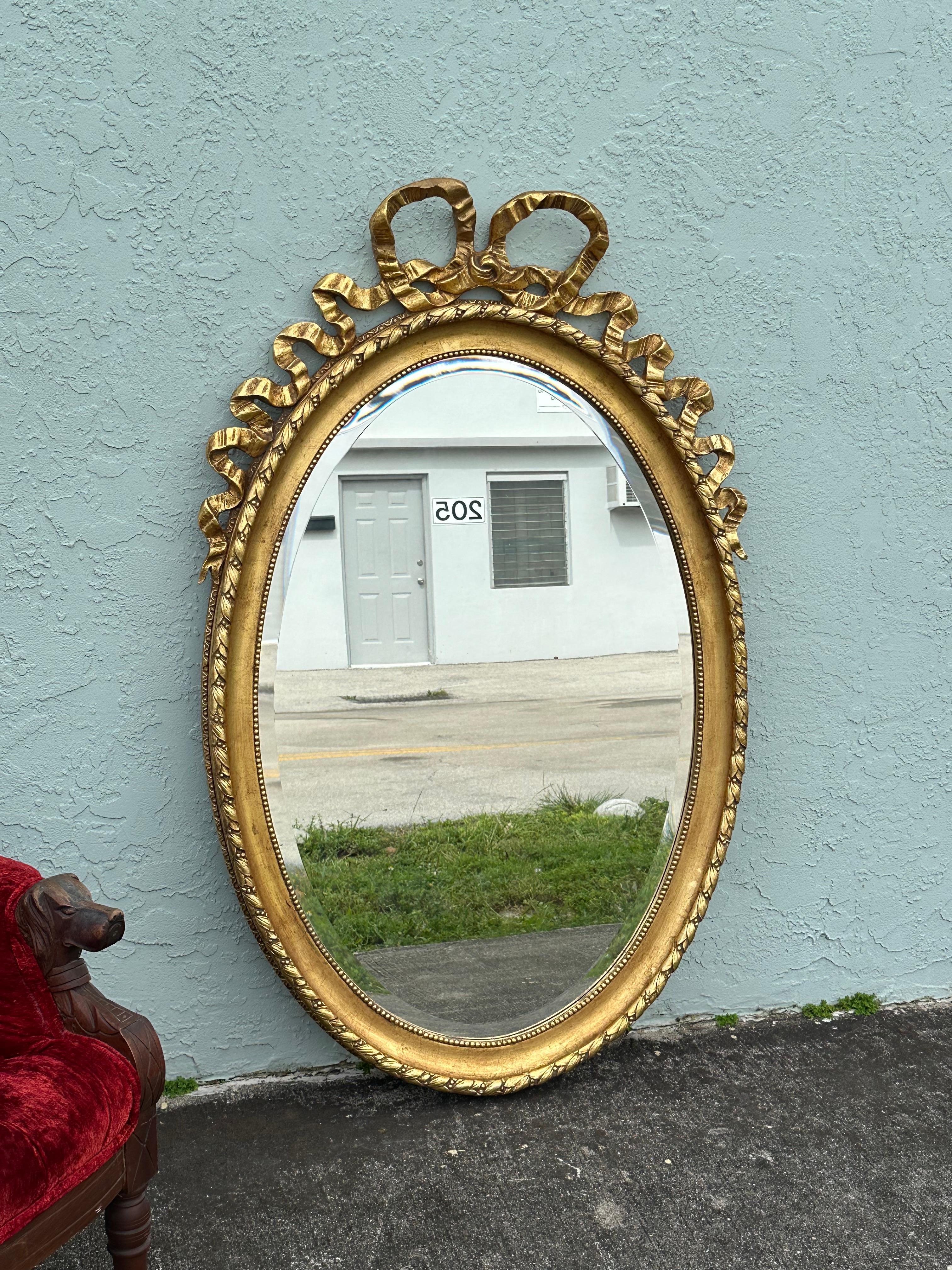Ce miroir ovale en bois doré de style Louis XVI de la fin du XIXe siècle présente une glace biseautée et un ruban noué classique entremêlé d'accents floraux. Le miroir est entouré d'une bordure de perles. Entre les bordures de perles se trouve un