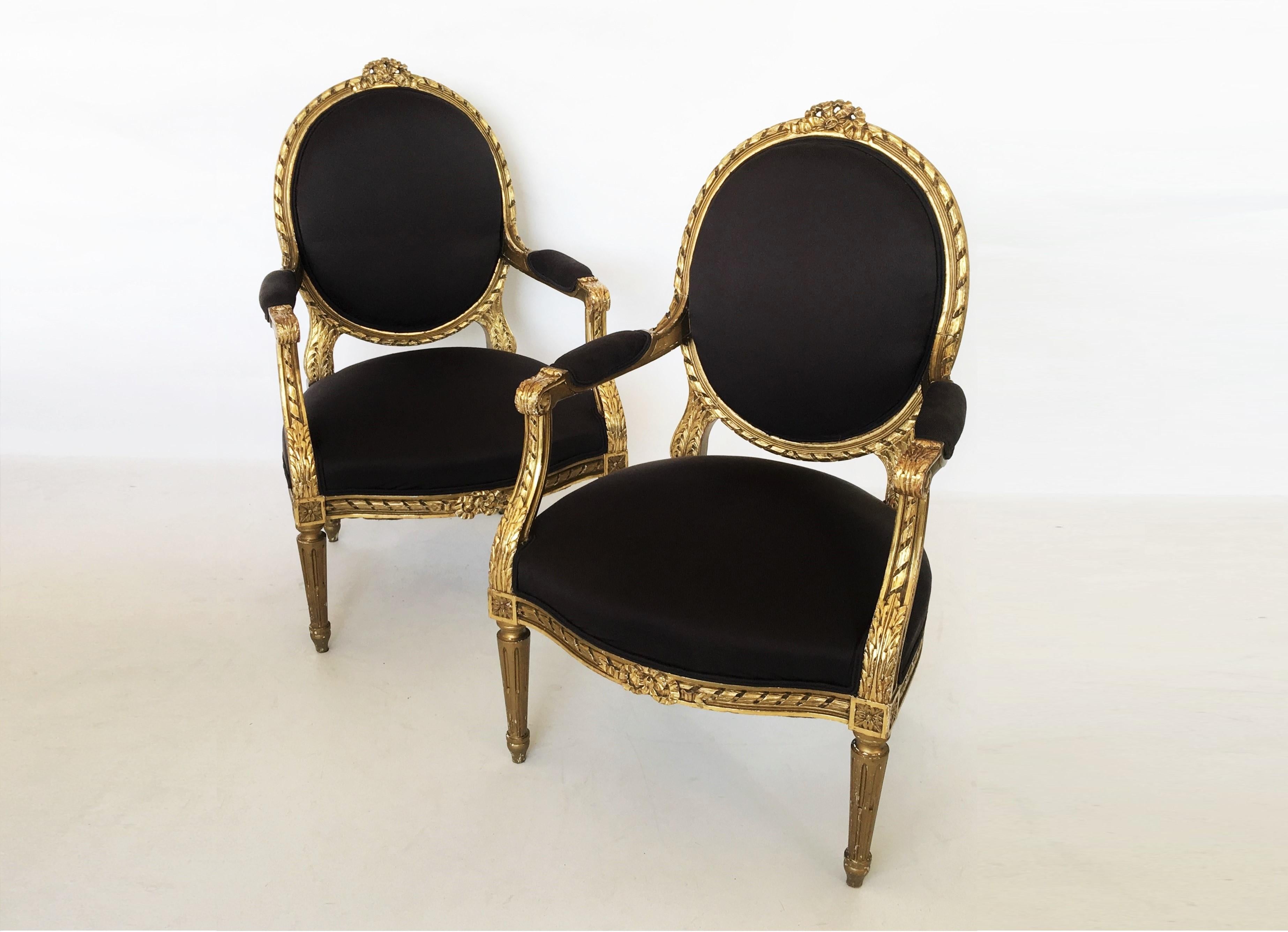 A magnificent pair of 19th-20th century Louis XVI style giltwood open armchairs of exceptional quality and scale. Each of the armchairs with elongated oval backs, carved frame banderole and knot moulding are beautifully designed with a top central