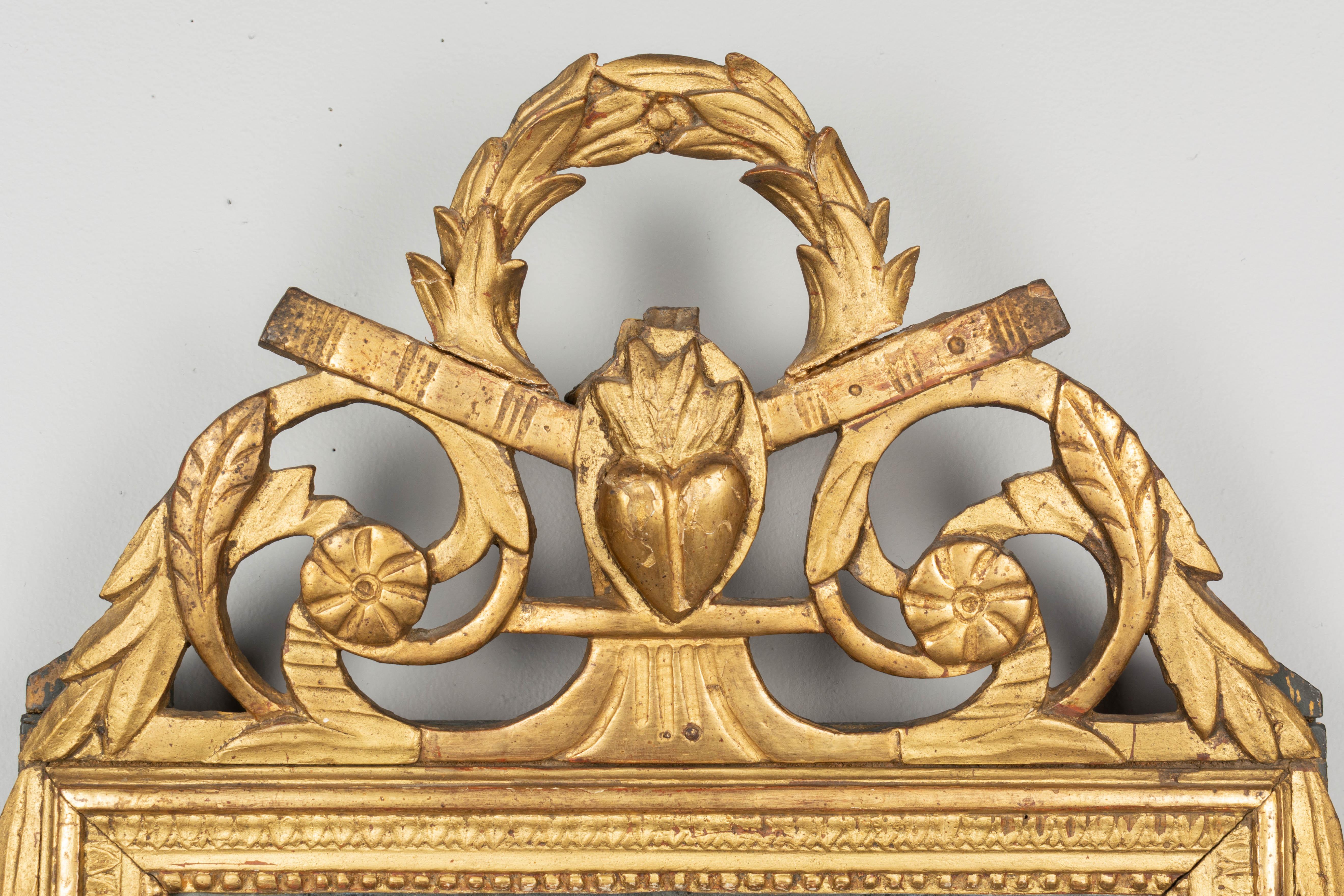 An early 19th century Louis XVI style French parcel giltwood bridal mirror from Provence. Nice hand carved crest with scrolling leaves and a flaming heart beneath a laurel wreath. All original with some restorations on the crest and some minor paint