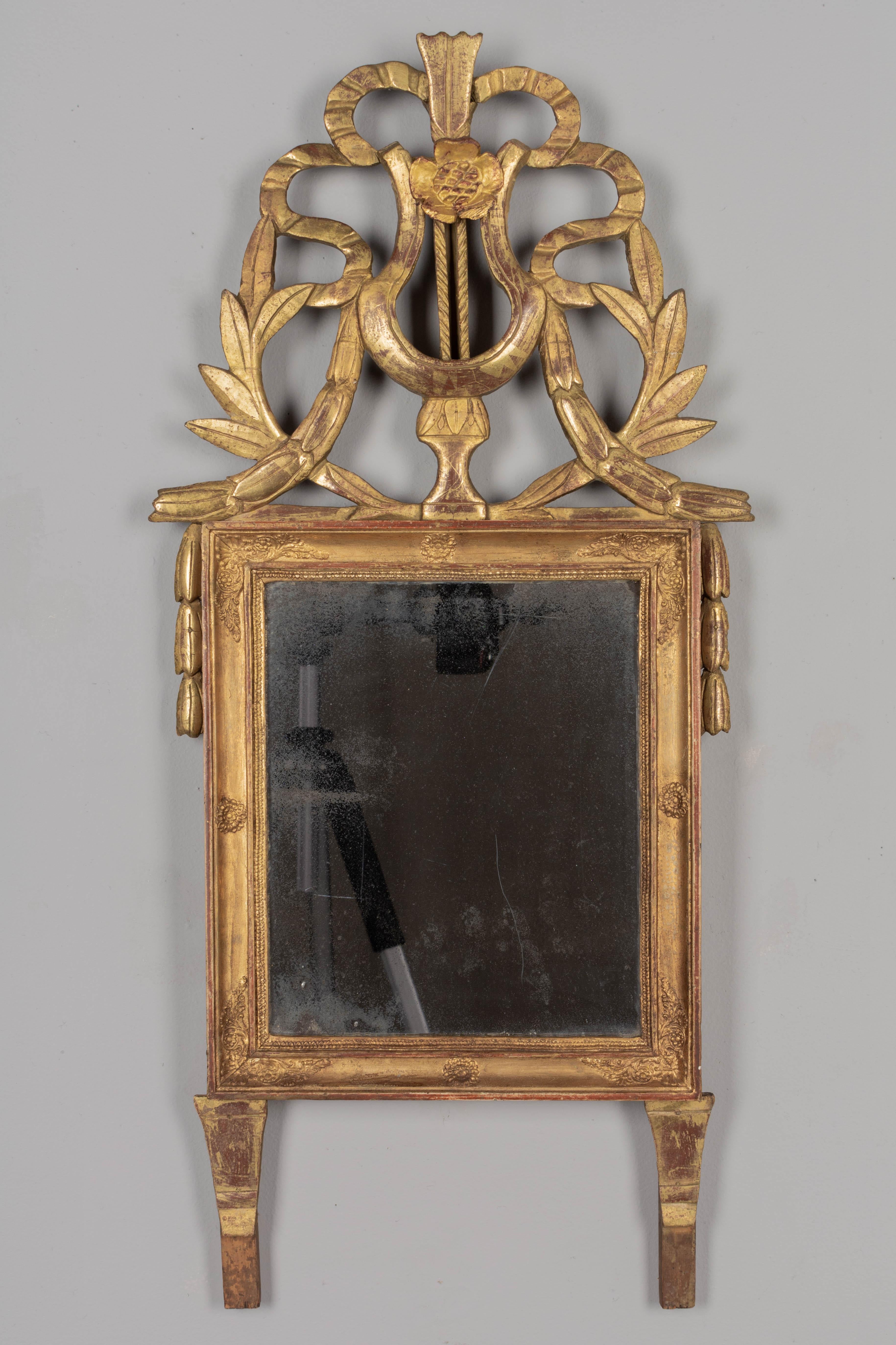 An early 19th century Louis XVI style French giltwood mirror. Large lyre shaped carved crest with ribbons and laurel leaves. All original with some restoration on the crest and minor losses. Warm gilt patina. A good antique mirror with old silvering