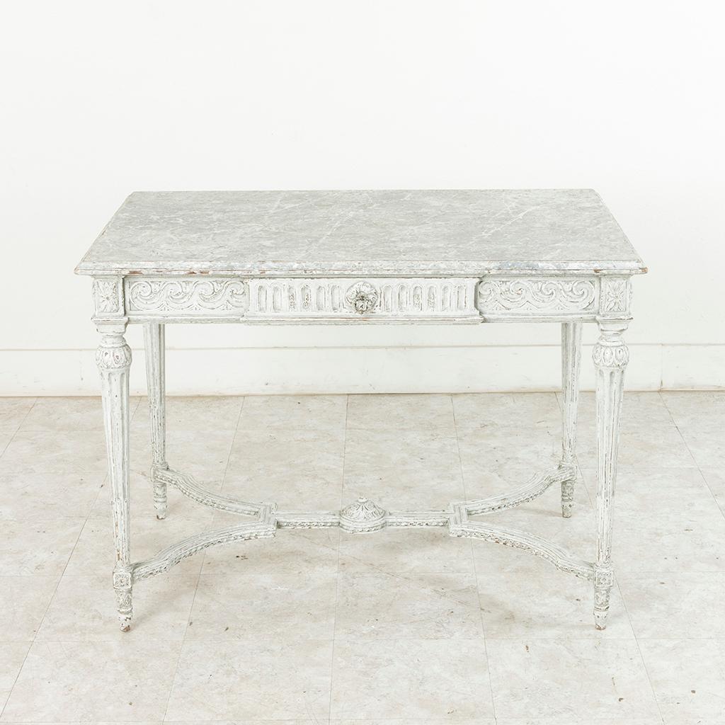 Found in France painted in a Gustavian grey, this French Louis XVI style hand-carved oak centre table from the late 19th century is finished on all sides and features a bevelled faux marble painted top. Carvings of scrolling and fluted arcades