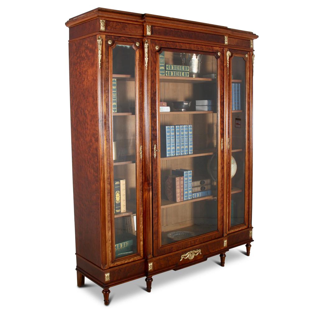 A French late-19th century Louis XVI style three door bookcase or vitrine in ‘plum pudding’ mahogany, the breakfront -profile case with finely-cast bronze ormolu mounts, the three doors with bevelled glass and opening to four sturdy oak adjustable