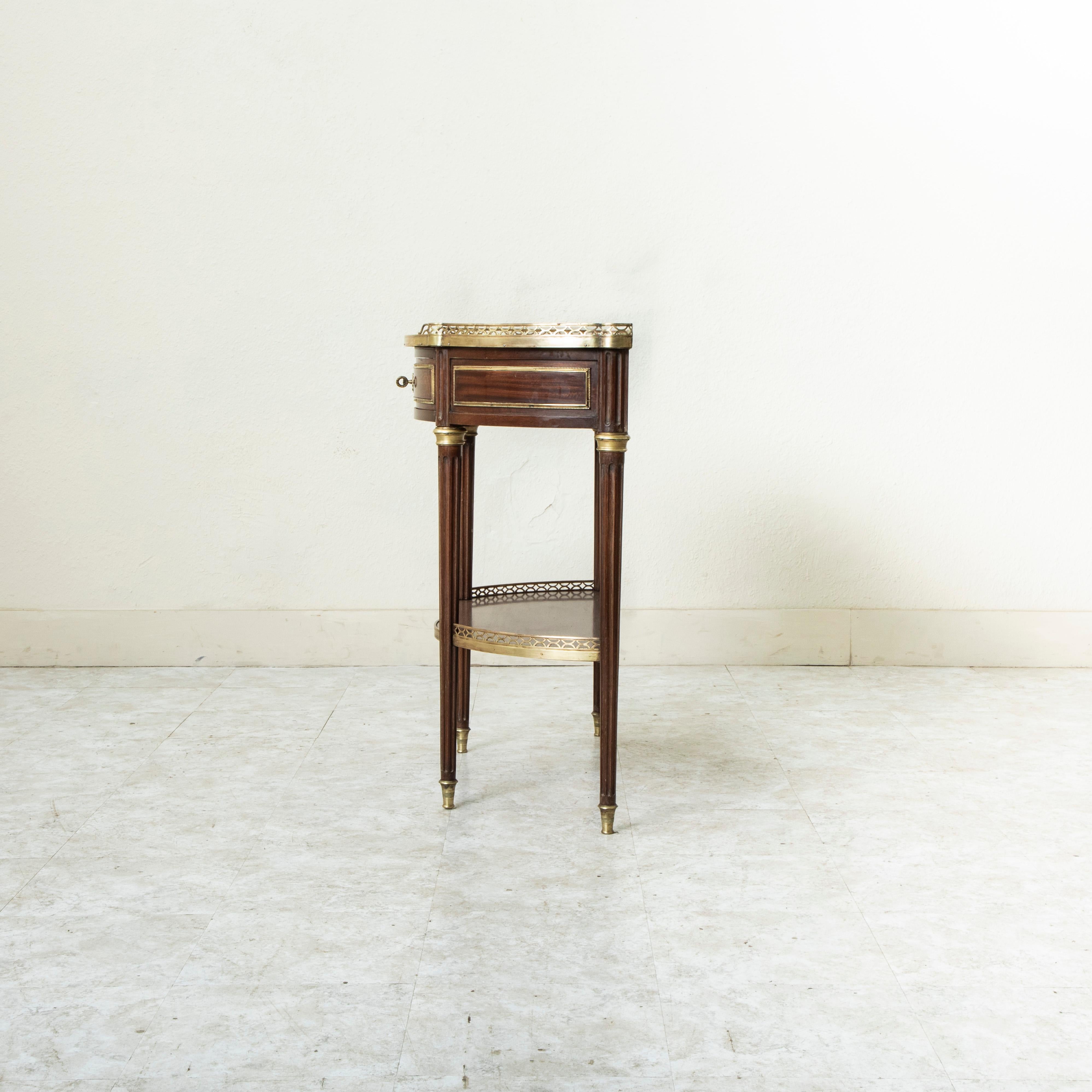 Cette console demi-lune en acajou de style Louis XVI français du milieu du XIXe siècle présente un plateau en marbre blanc entouré d'une galerie en bronze percée. Les panneaux du tablier sont ornés d'une bande de bronze et de perles. Un seul tiroir