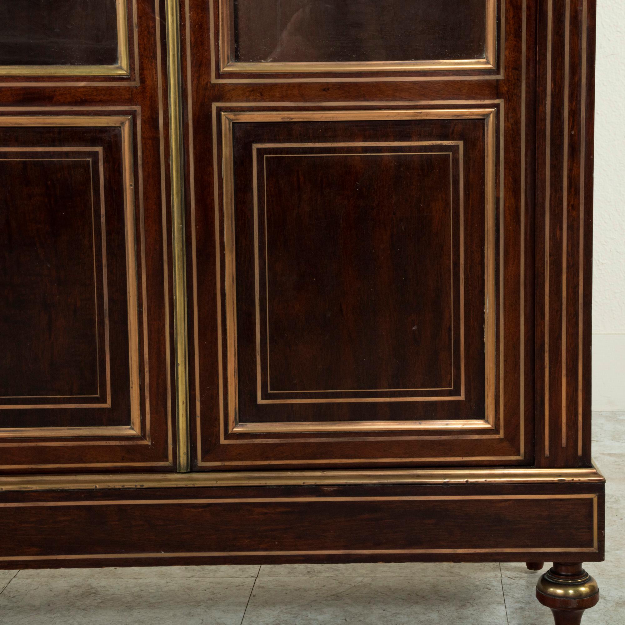 Standing at 63 inches in height, this small scale mid-nineteenth century Louis XVI style mahogany bibliotheque or bookcase is finished with stunning bronze banding. Its corners feature fluting with inset bronze filets. Both doors have their original