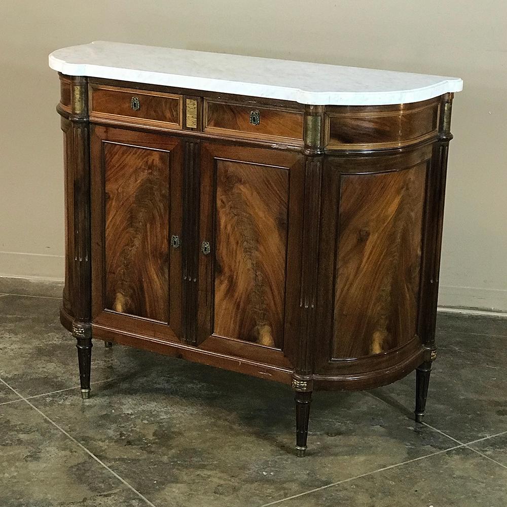 19th century French Louis XVI style marble-top buffet showcases the sheer natural beauty of the exotic imported flame mahogany that appears on the cabinet doors, even on the rounded sides. Brass accents with a touch of neoclassical flair add