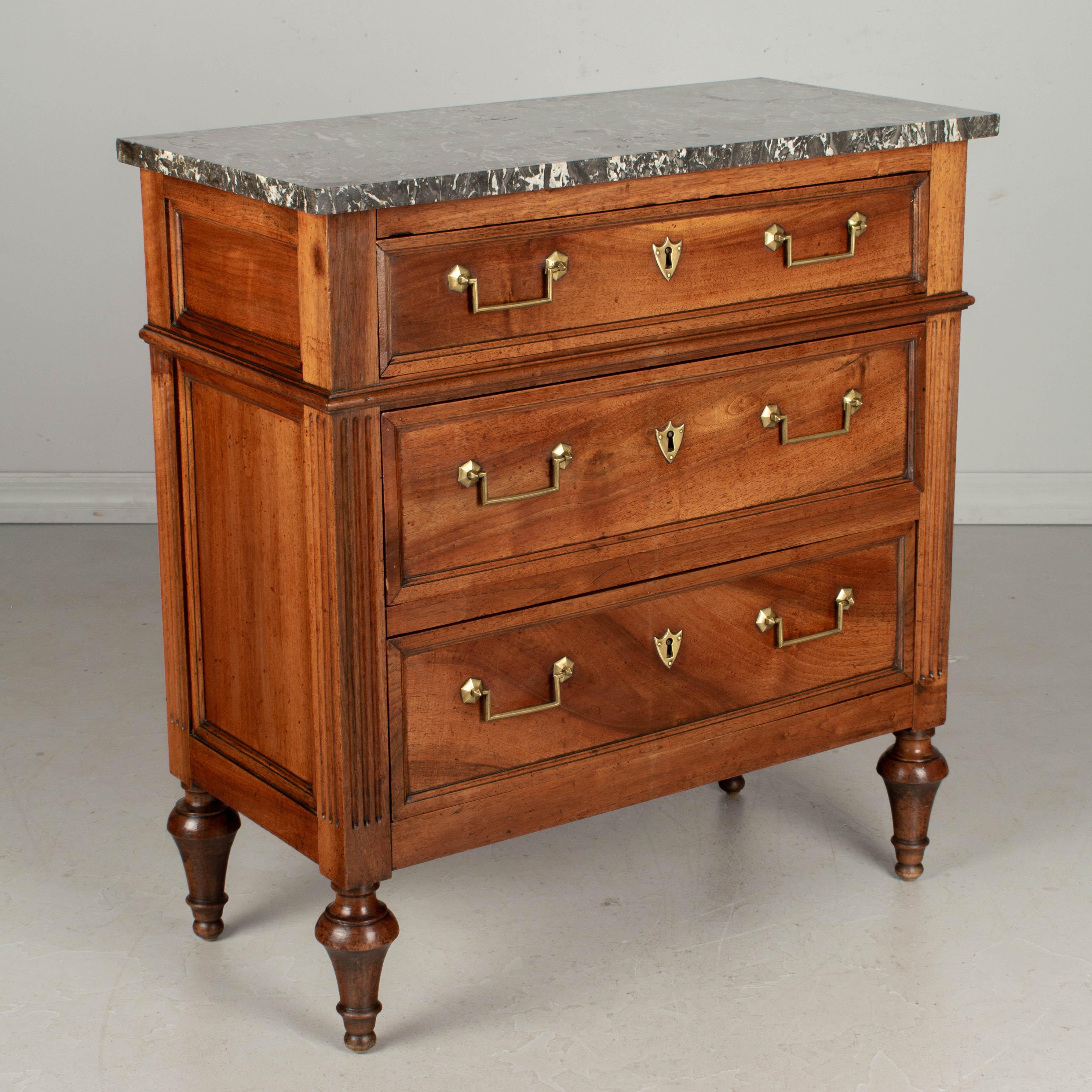 A fine 19th century Louis XVI French commode, or chest of drawers, made of solid walnut with gray St. Anne marble top. Three dovetailed drawers with original brass hardware and locks, but no keys. Subtle details include paneled sides, fluted front