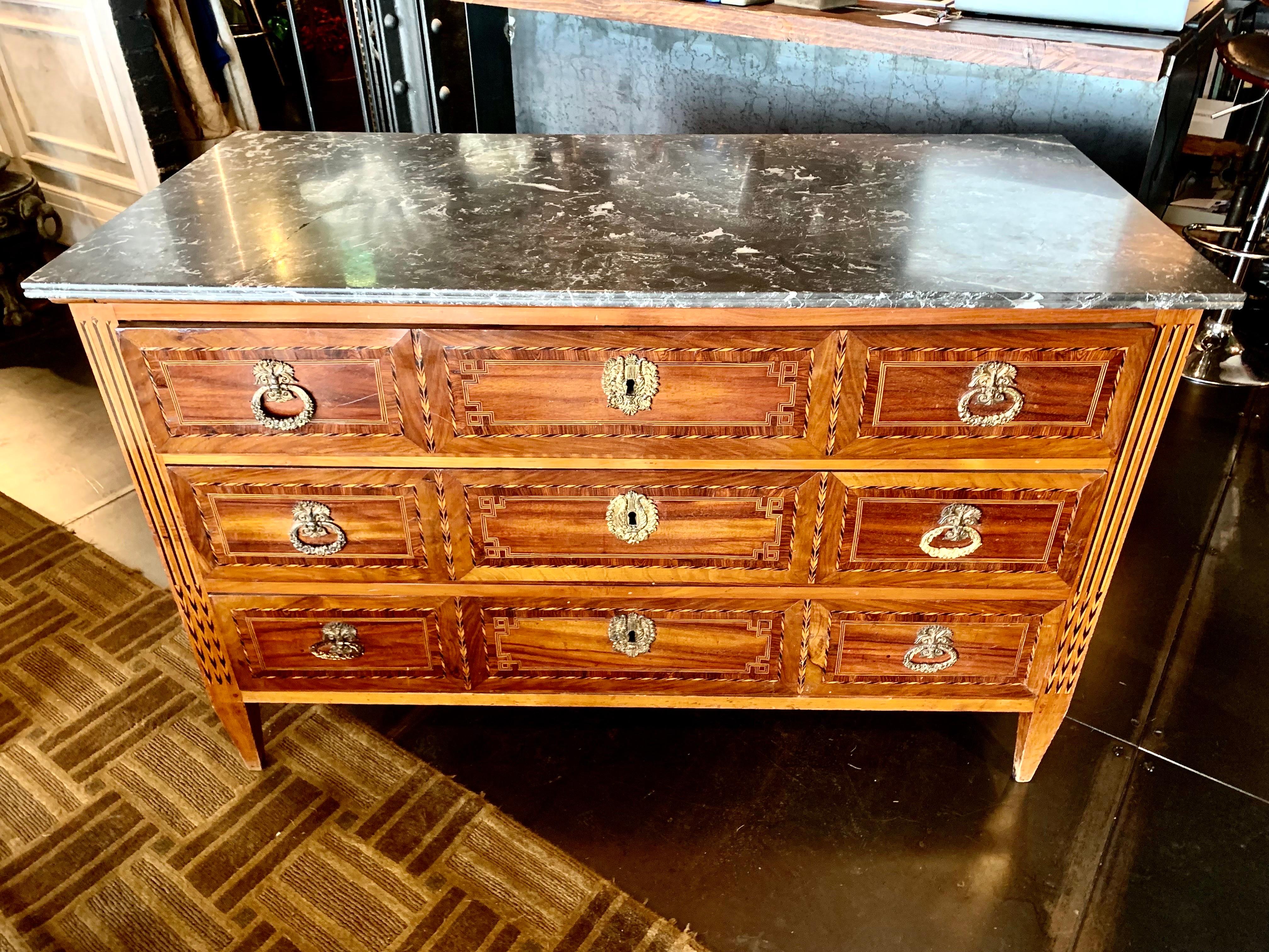 French chest of drawers from the early 19th century, Louis XVI style, in walnut with different types of wood marquetry, with lime Wood and and black bog oak, has three drawers with bronze handles and keyholes, the top rd dr dark gray marble edged