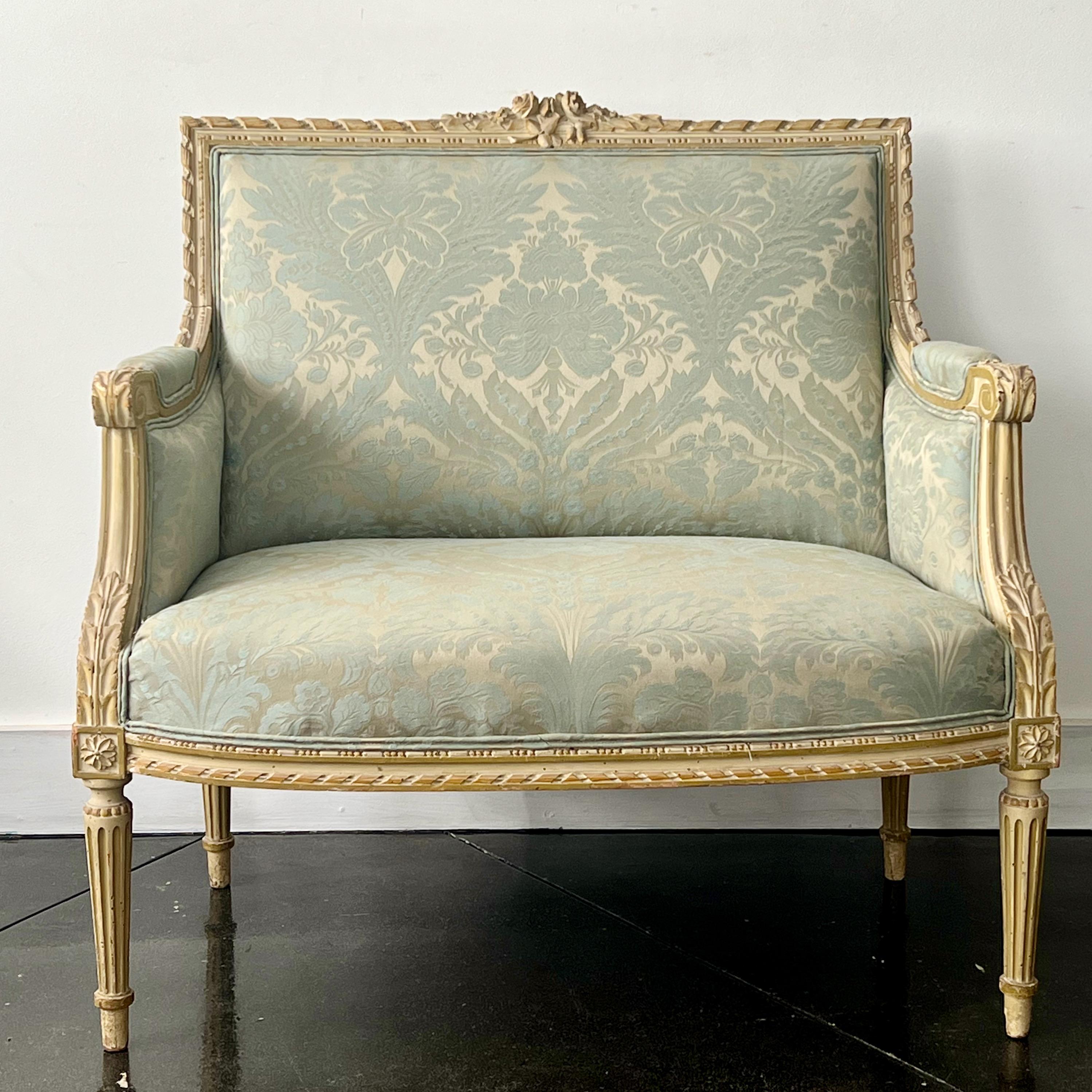19th century French Louis XVI style bergère marquise upholstered armchair in painted wood frame with neoclassical architecture embellished hand-carved foliates, rosettes and tapered and fluted legs. Newly upholstered in floral damask. 
A classic