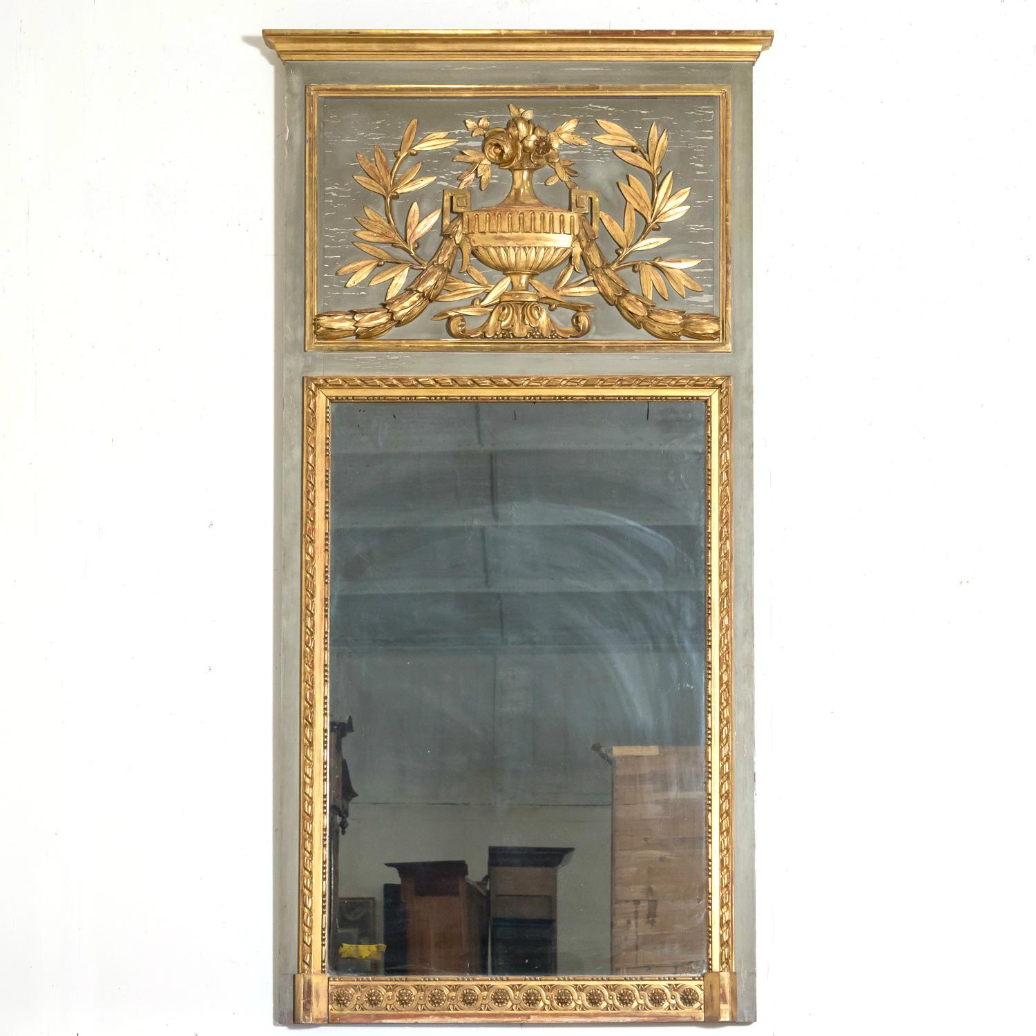 A 19th century French Louis XVI style painted and and parcel gilt trumeau mirror, circa 1870s. The greenish-gray patinated frame, adorned with neoclassical relief carvings, speaks to the attention to detail and craftsmanship of the era. The