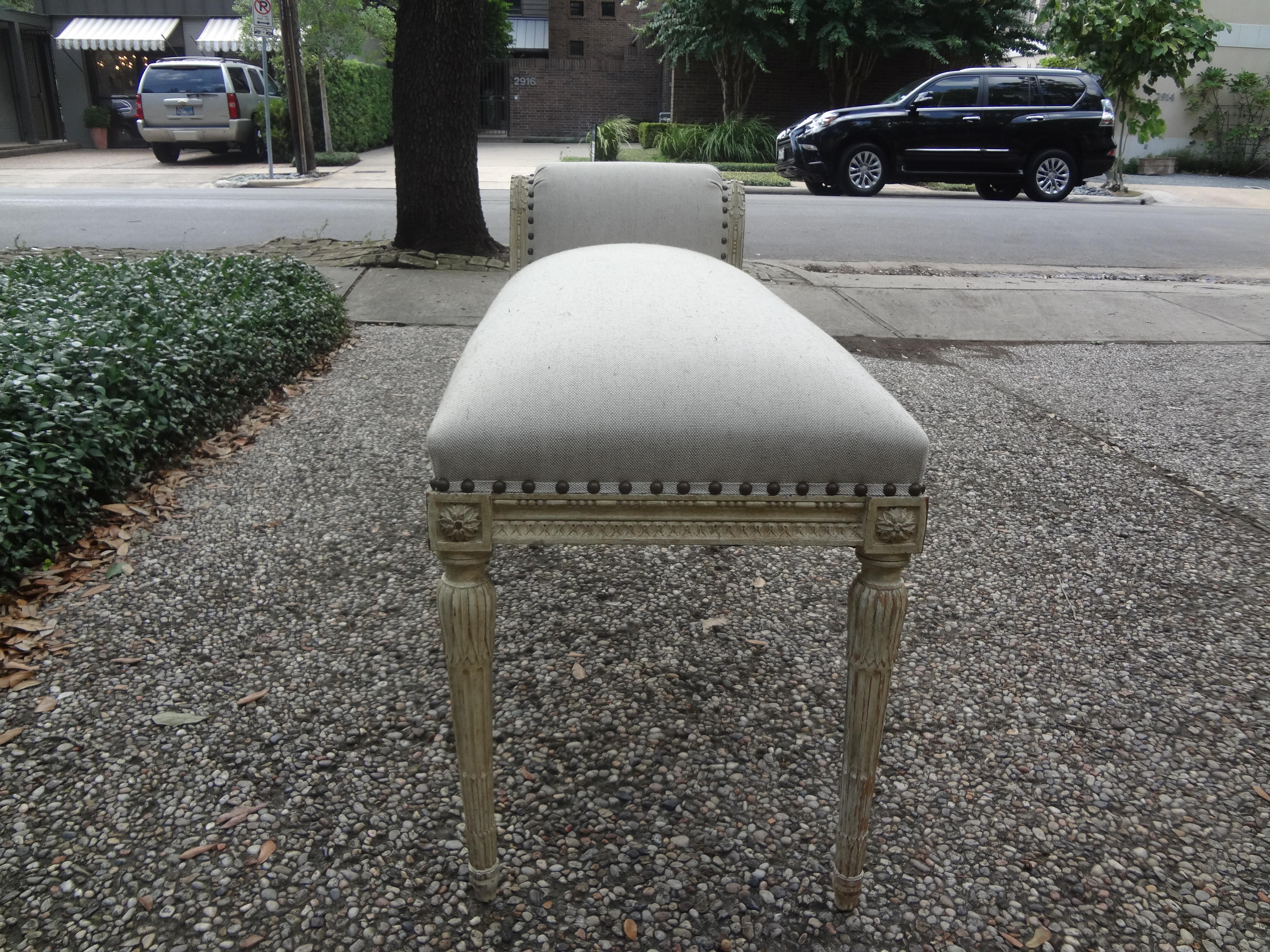 Stunning 19th century French Louis XVI style painted bench. This unusual antique French Louis XVI style painted one-arm bench has been taken down to the frame and professionally upholstered in oatmeal colored linen with spaced brass nailhead