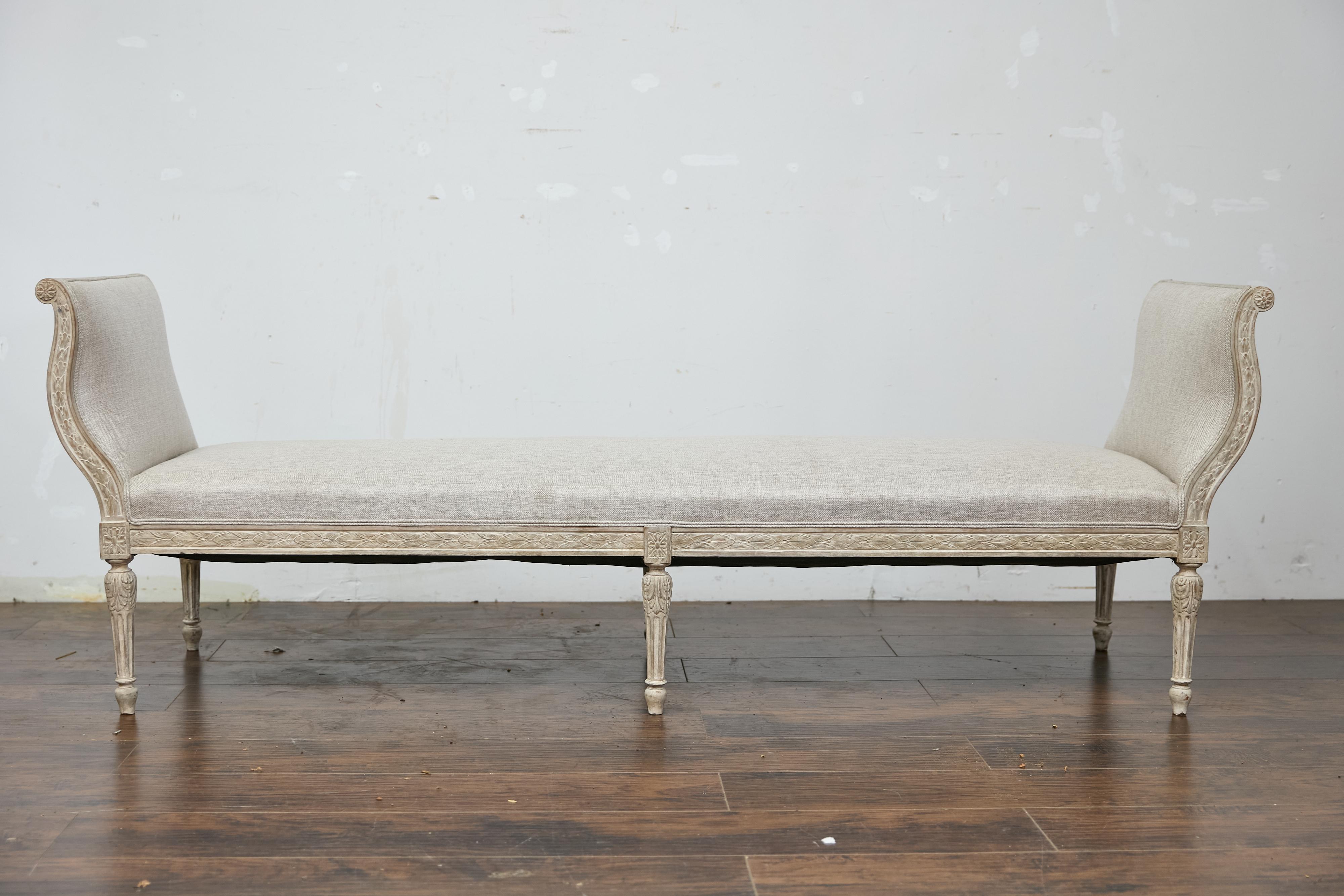 A French Louis XVI style painted wood daybed from the 19th century with foliage carved decor and custom upholstery. This 19th-century French Louis XVI style painted wood daybed embodies elegance and refinement, featuring an intricately carved