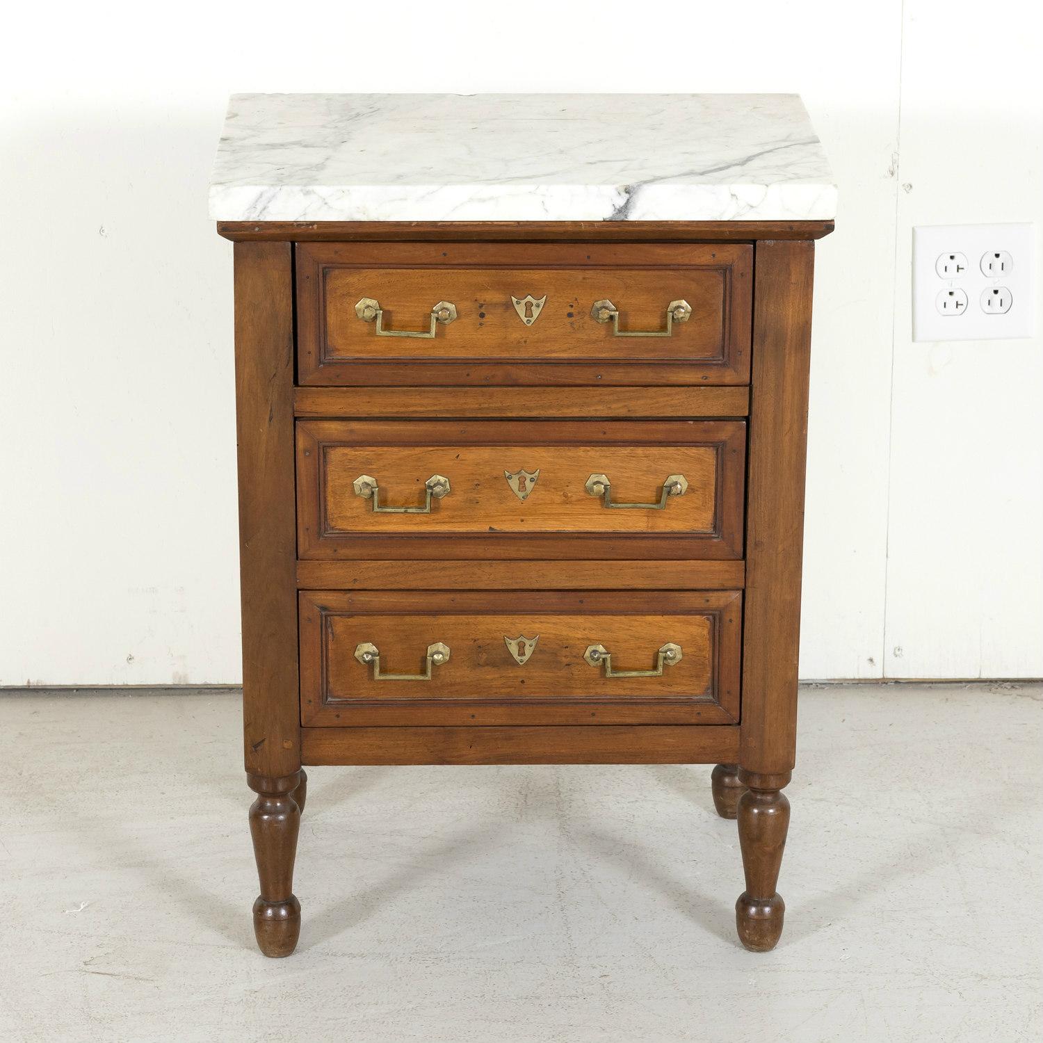 A 19th century French Louis XVI style petite commode handcrafted of walnut near Villeneuve les Avignon in the South of France, circa 1850s. Having a thick rectangular Carrara marble top over three drawers with the original neoclassical drop bail