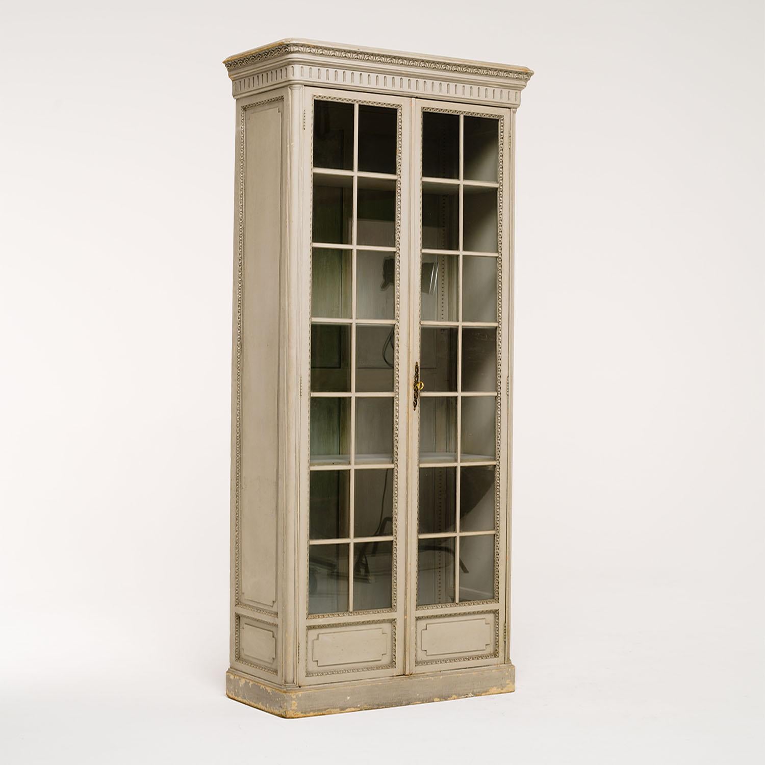 A tall, antique French Louis XVI style bookcase made of hand crafted painted Pinewood, in good condition. The library cabinet, cupboard is composed with two slightly smoked, paned glass doors, the inside consist three adjustable shelfs. The buffet