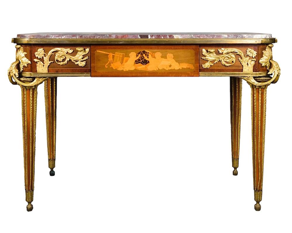 19th century French center table of the highest quality after the original model by Jean-Henri Riesener (1734-1806), with variegated rouge marble top, elaborate foliate ormolu mounts, frieze decorated with exceptional fruitwood marquetry inlay of