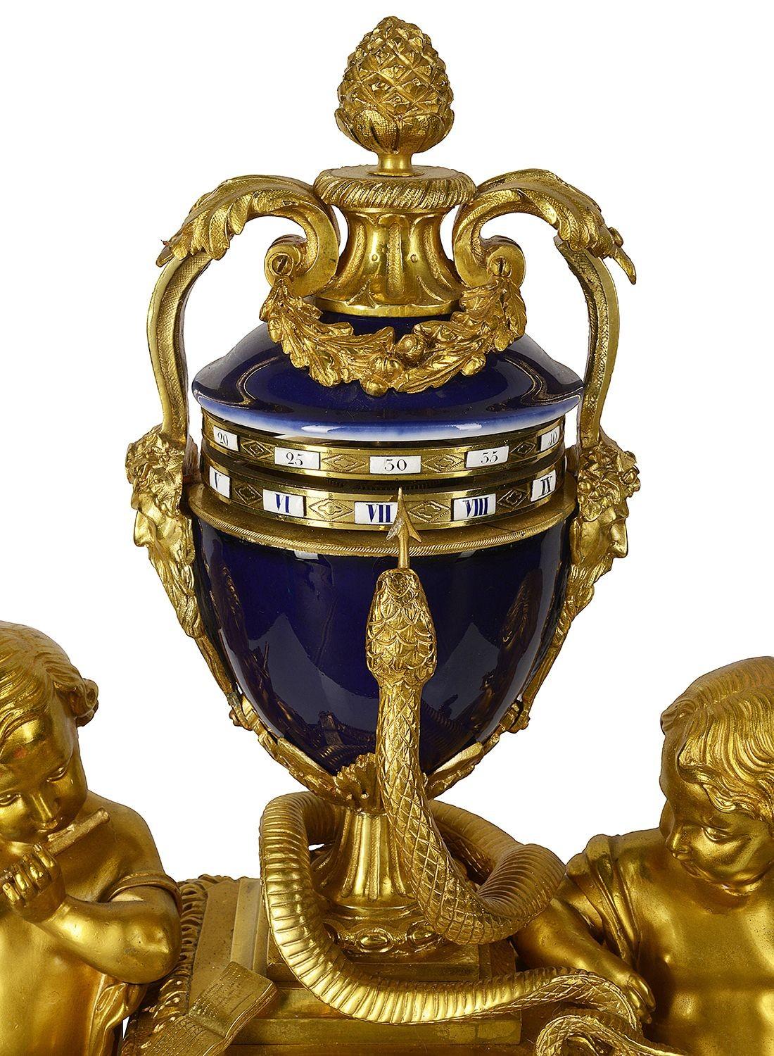 A wonderful late 19th century French Annular Louis XVI style gilded ormolu revolving mantel clock, depicting putti representing the arts and music, either side of a rotating tole urn with Roman enamel numerals and a Serpent that indicates the time.
