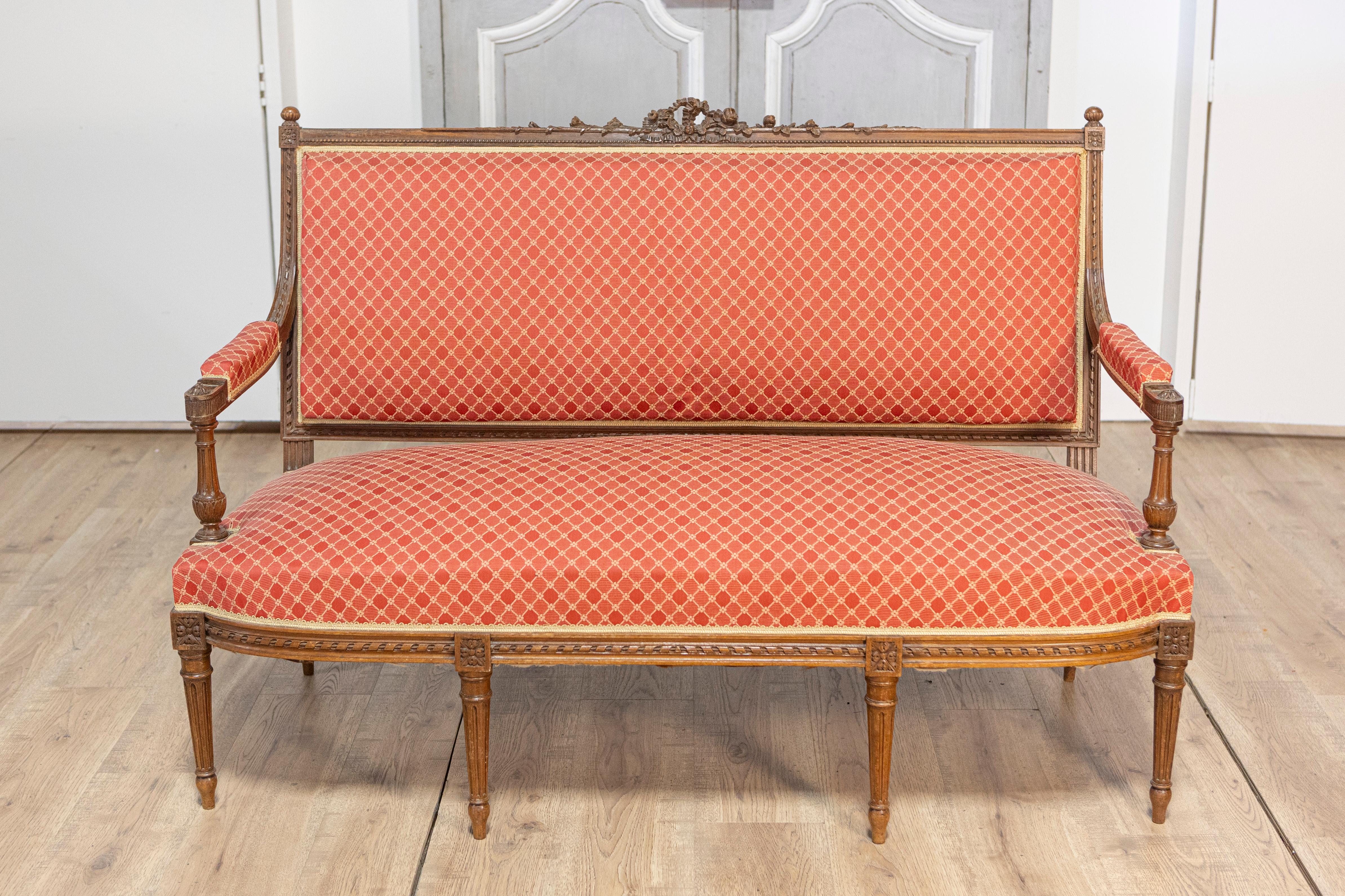 Questo squisito divano francese in stile Luigi XVI del XIX secolo, circa 1860, esemplifica l'eleganza e la raffinatezza del design classico francese. Realizzata in noce massiccio, la cornice è intricatamente intagliata con delicati motivi floreali e