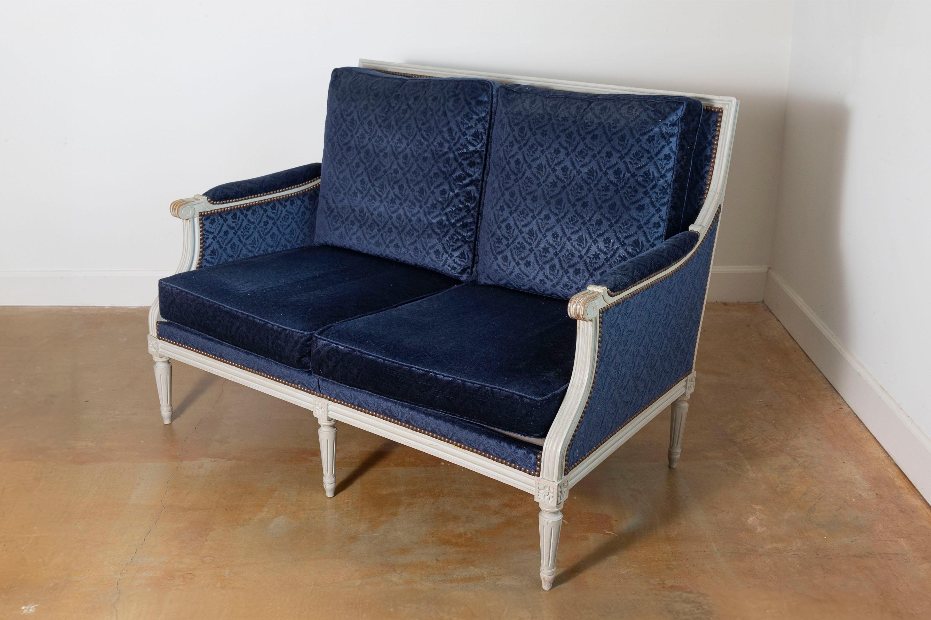 Este sofá francés del siglo XIX de estilo Luis XVI es sinónimo de elegancia y artesanía atemporal. La estructura de madera tallada, pintada en un tono suave y apagado, presenta elementos de diseño clásicos de Luis XVI, como patas estriadas,