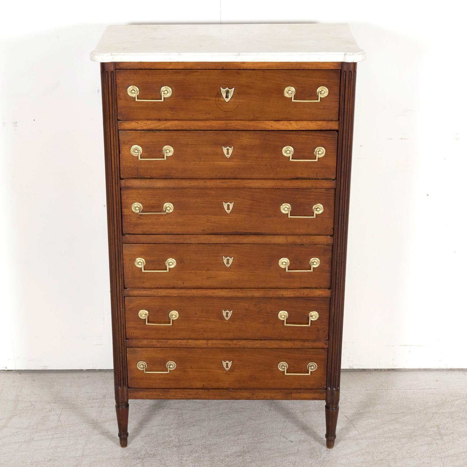 A handsome early 19th century French Louis XVI style chiffonier or tall gentleman's chest, circa 1810s, having a molded Carrara marble top with cookie cutter corners sitting atop six drawers adorned with original brass drop bail handles with stars